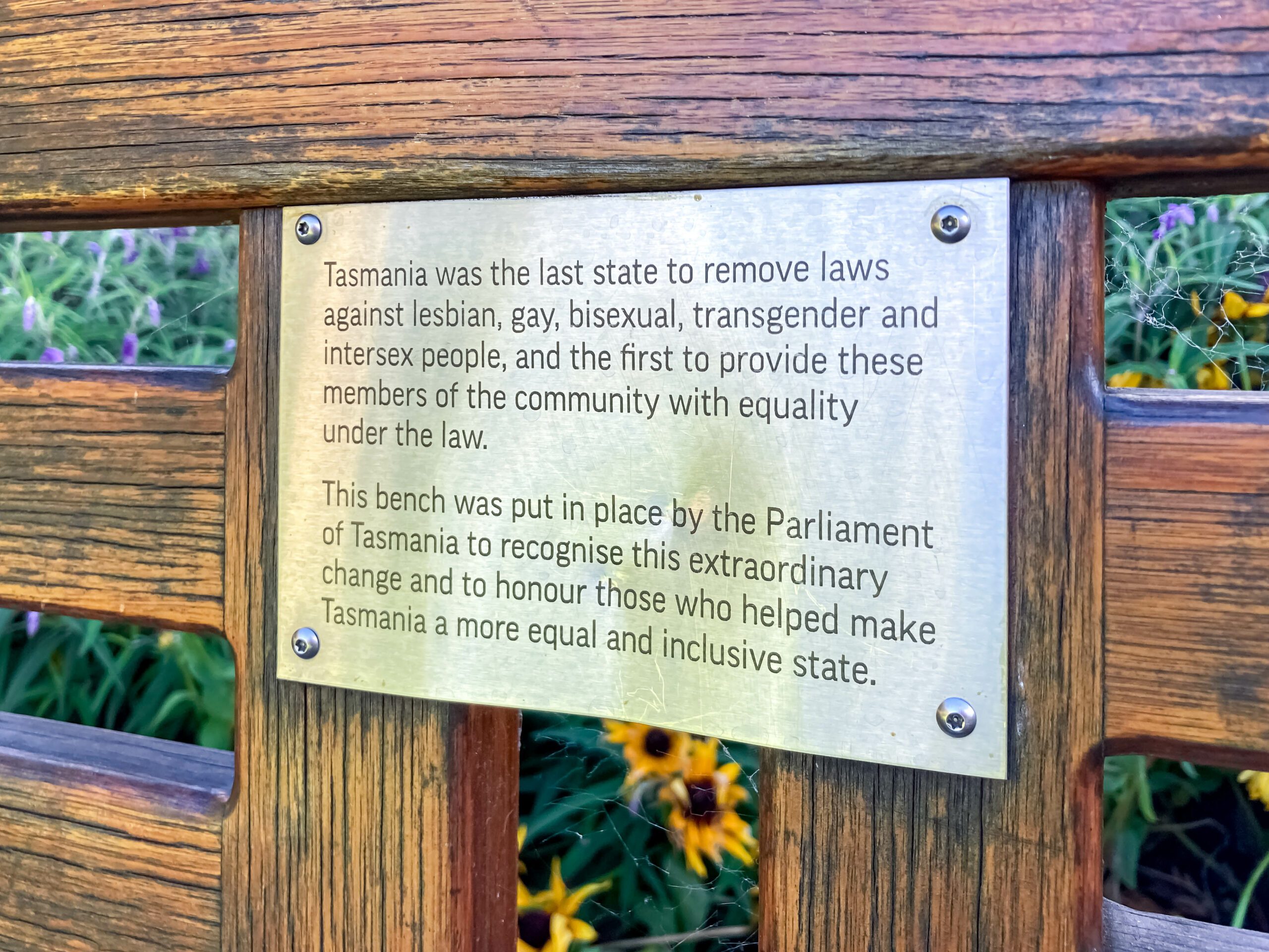 A brass plaque attached to a wooden bench recognising Tasmania as the last state to remove laws against lesbian, gay, bisexual, transgender and intersex people and the first to provide these members of the community with equality under the law