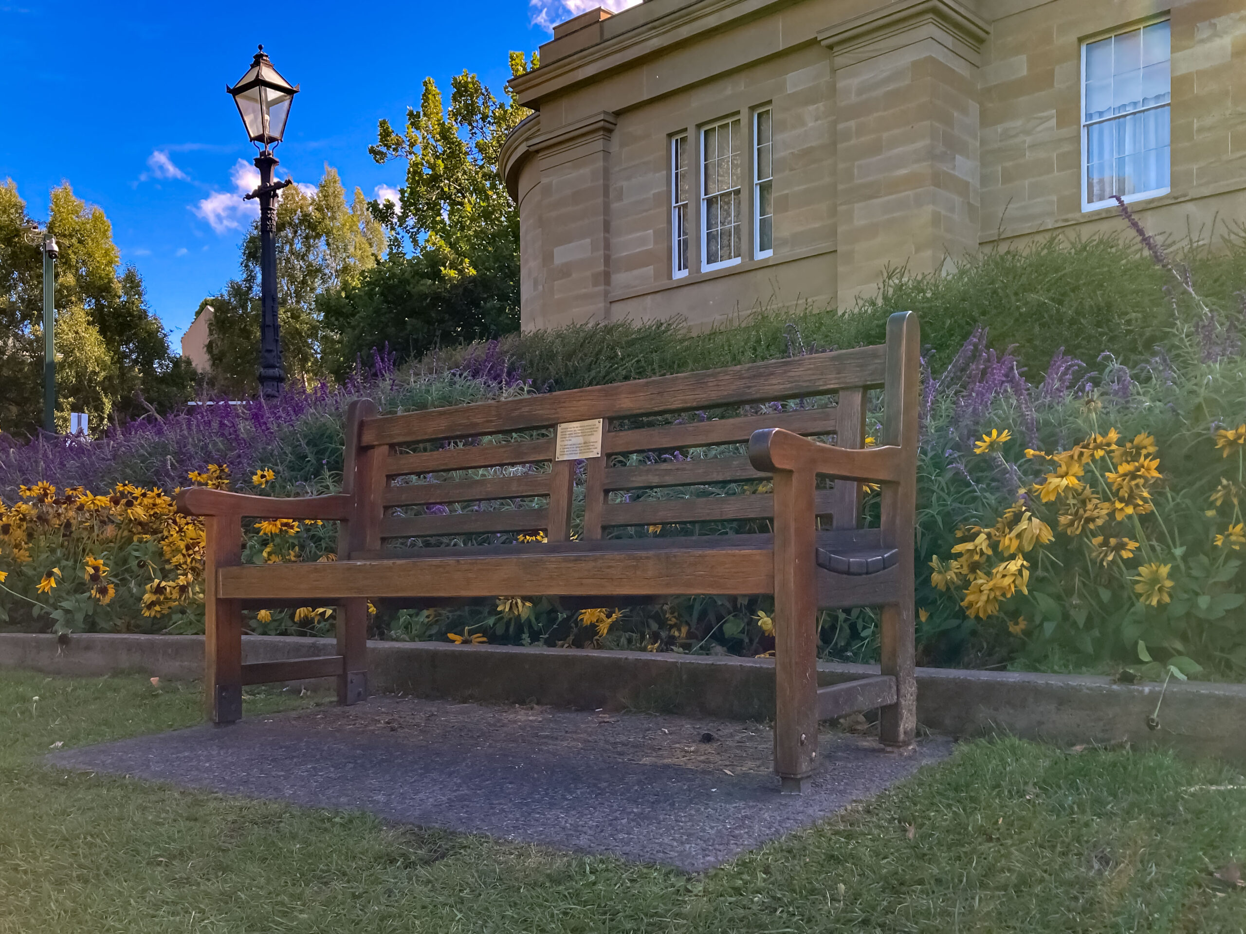 A wooden park bench in a garden outside of an old sandstone building