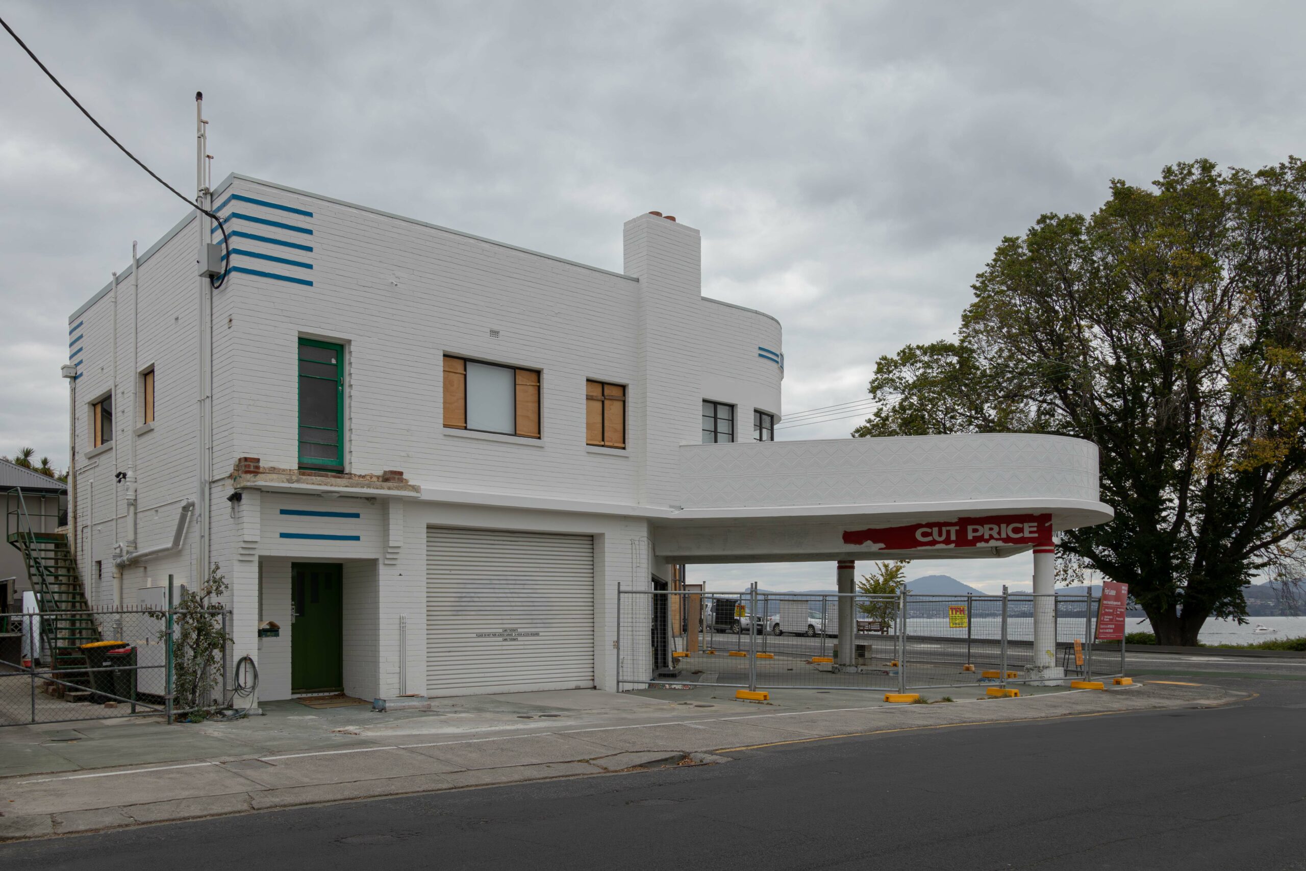 Side view of an art deco service station painted white. The first floor windows are boarded up
