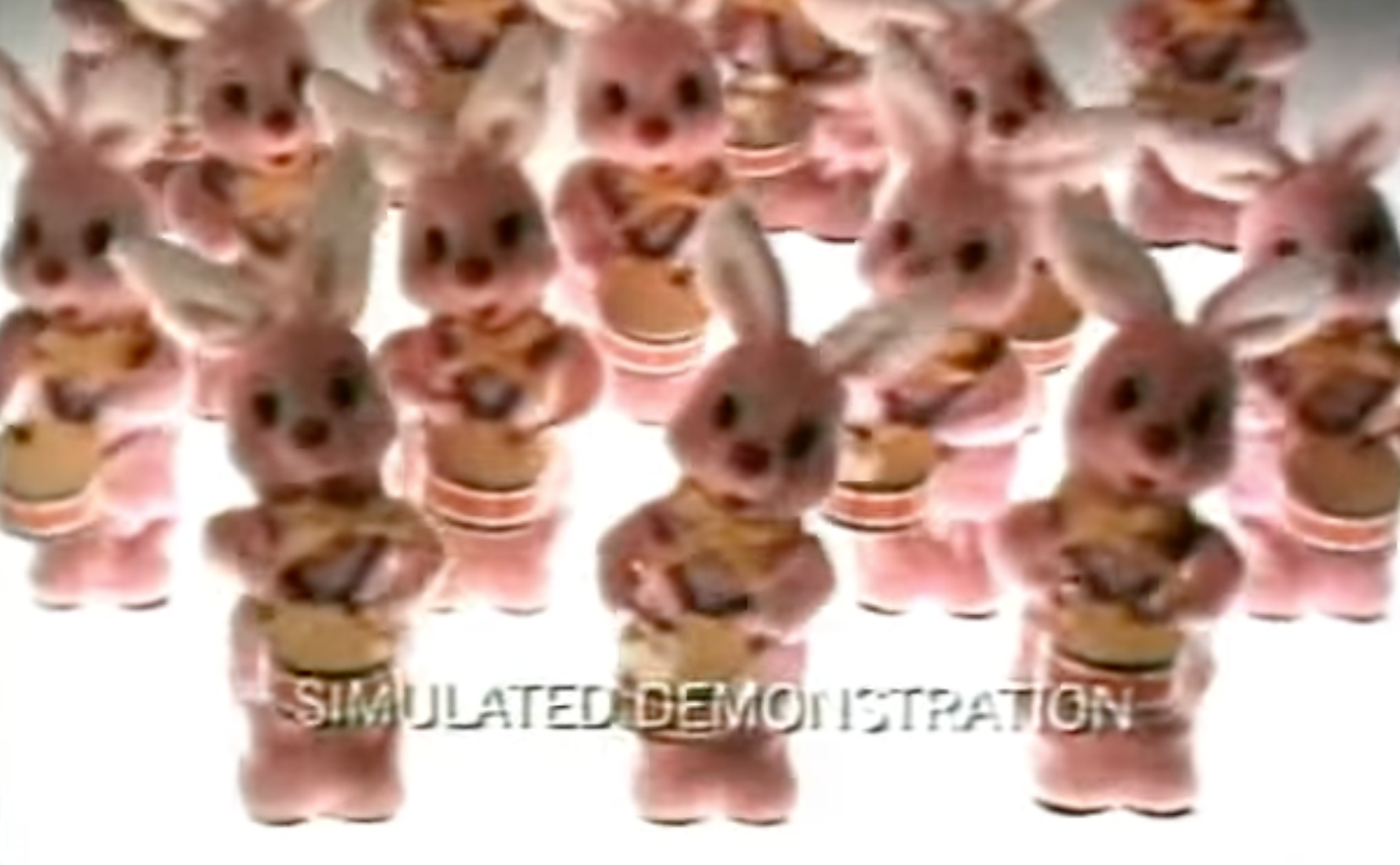 A collection of pink soft toy rabbits playing drums. Words across the bottom of the screen read "SIMULATED DEMONSTRATION"