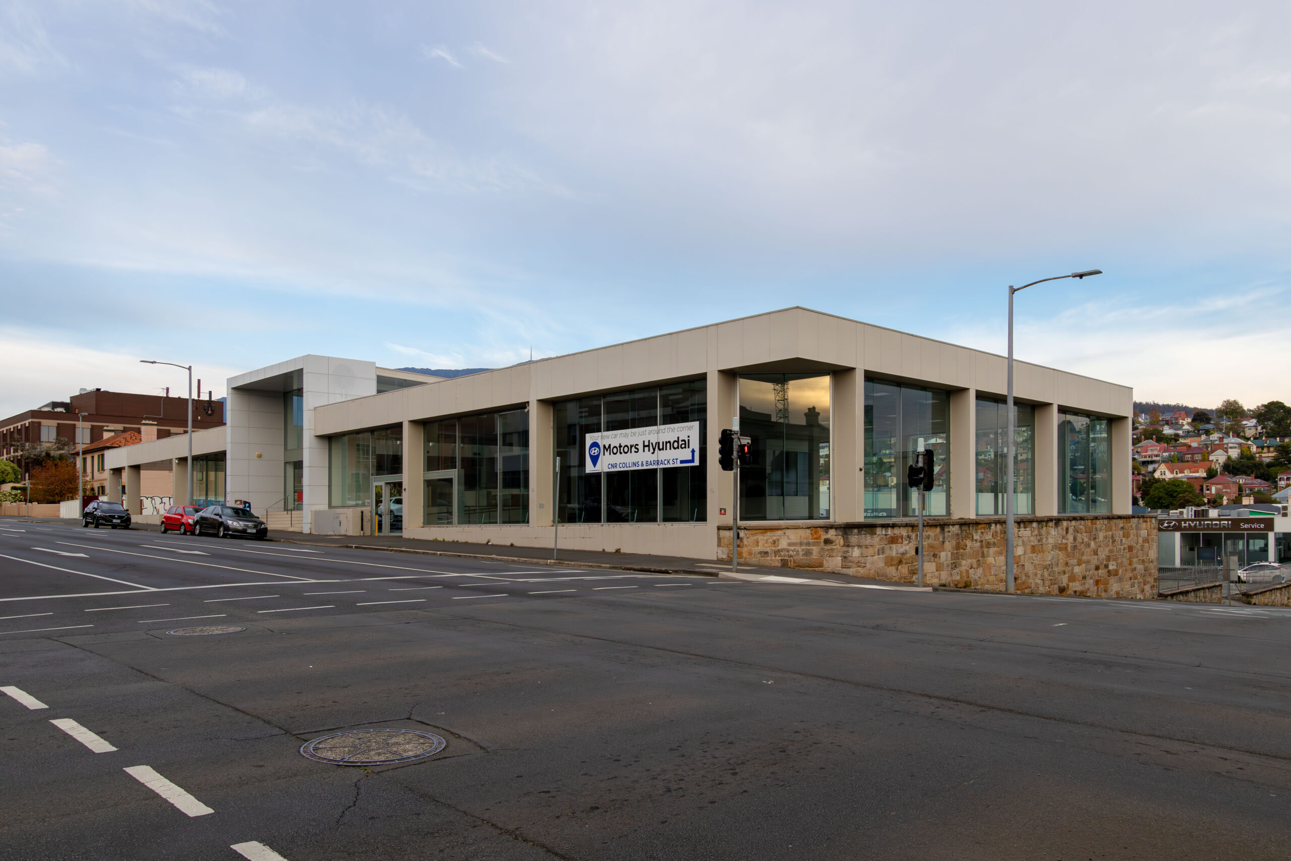 An empty former car dealership on an empty street. The glass walls sit atop a low sandstone wall