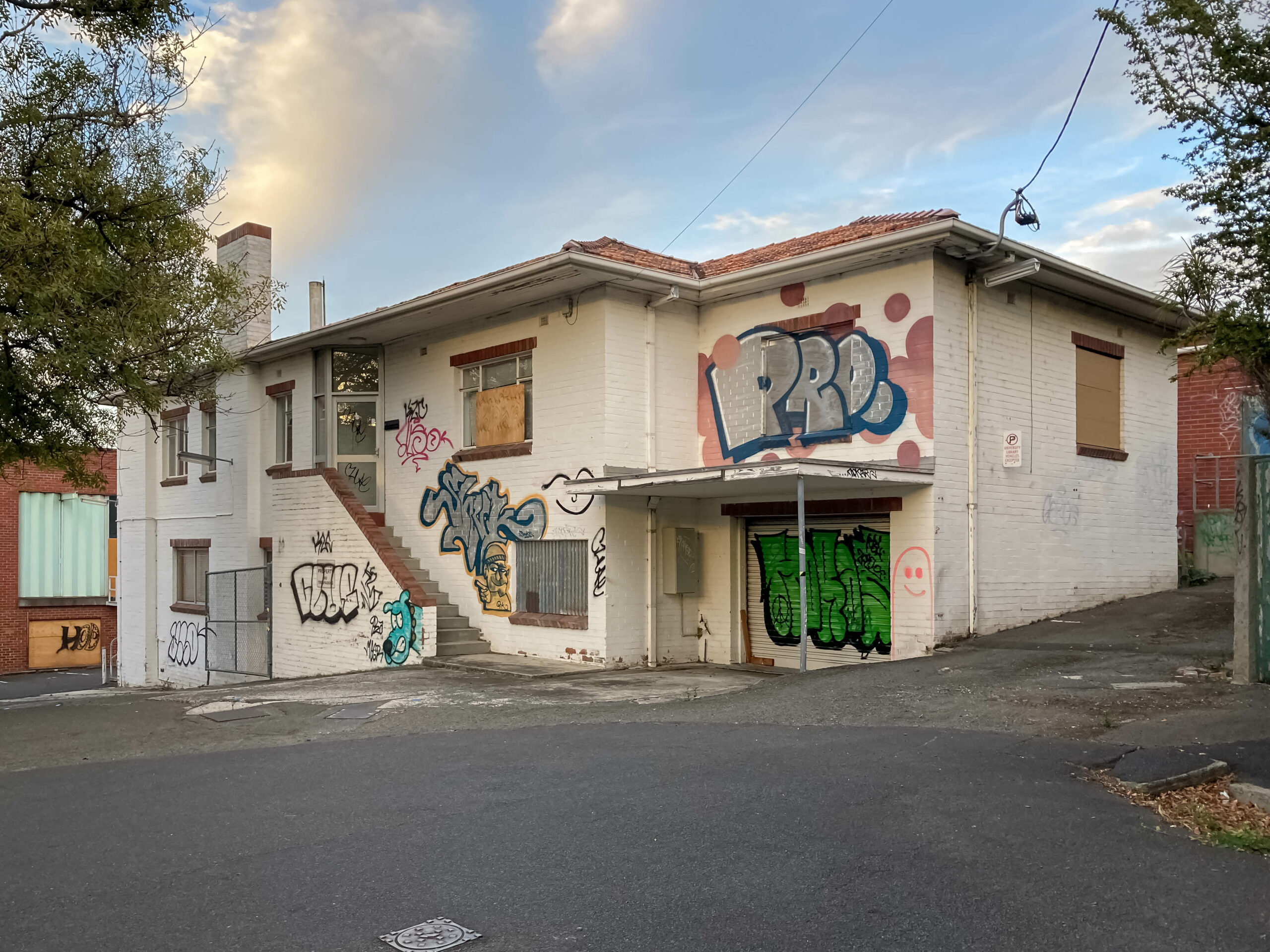 An old white brick two-storey house tagged with graffiti