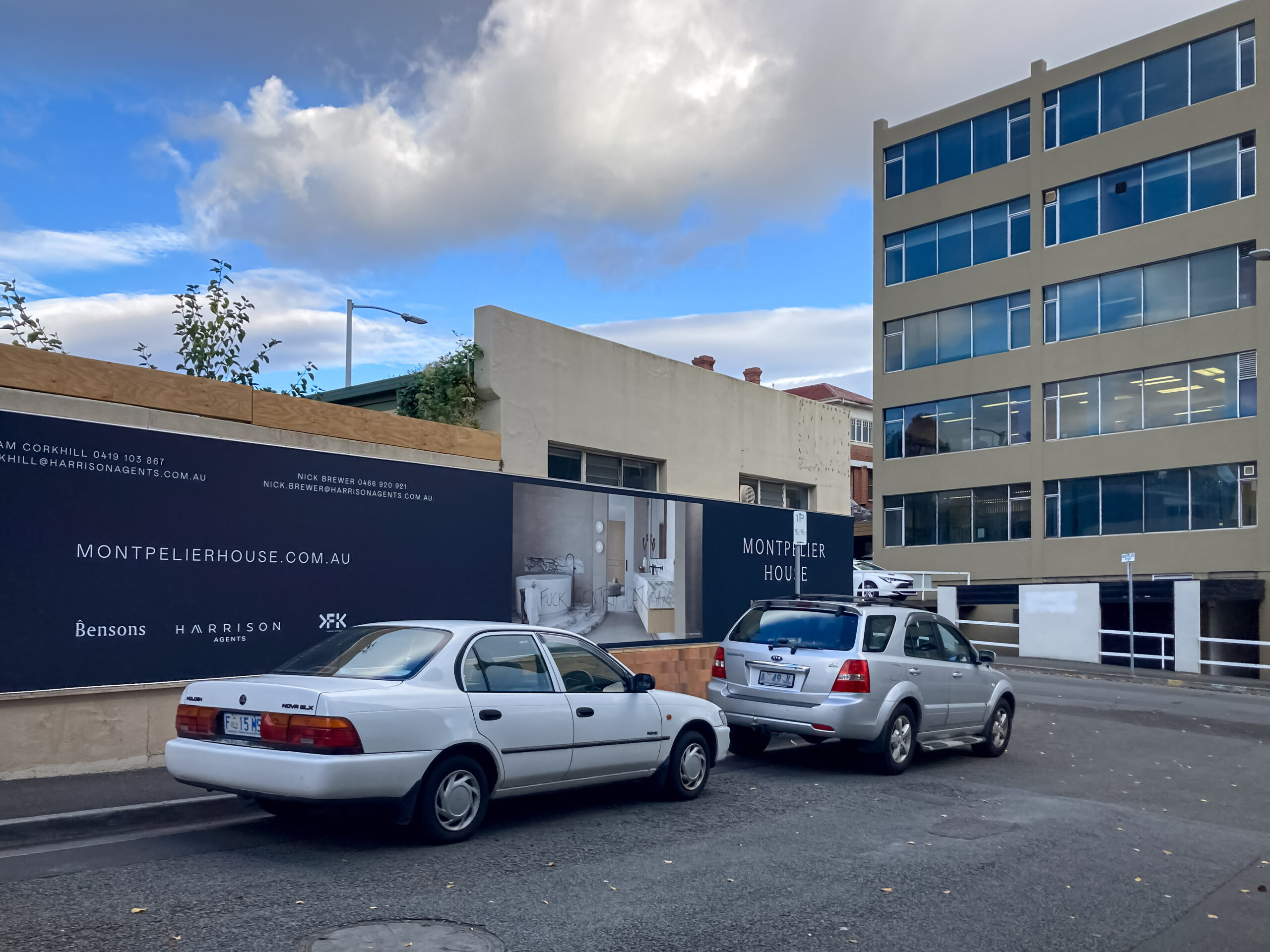 a low concrete building surrounded by advertising for a new apartment complex. Two cars are parked in front