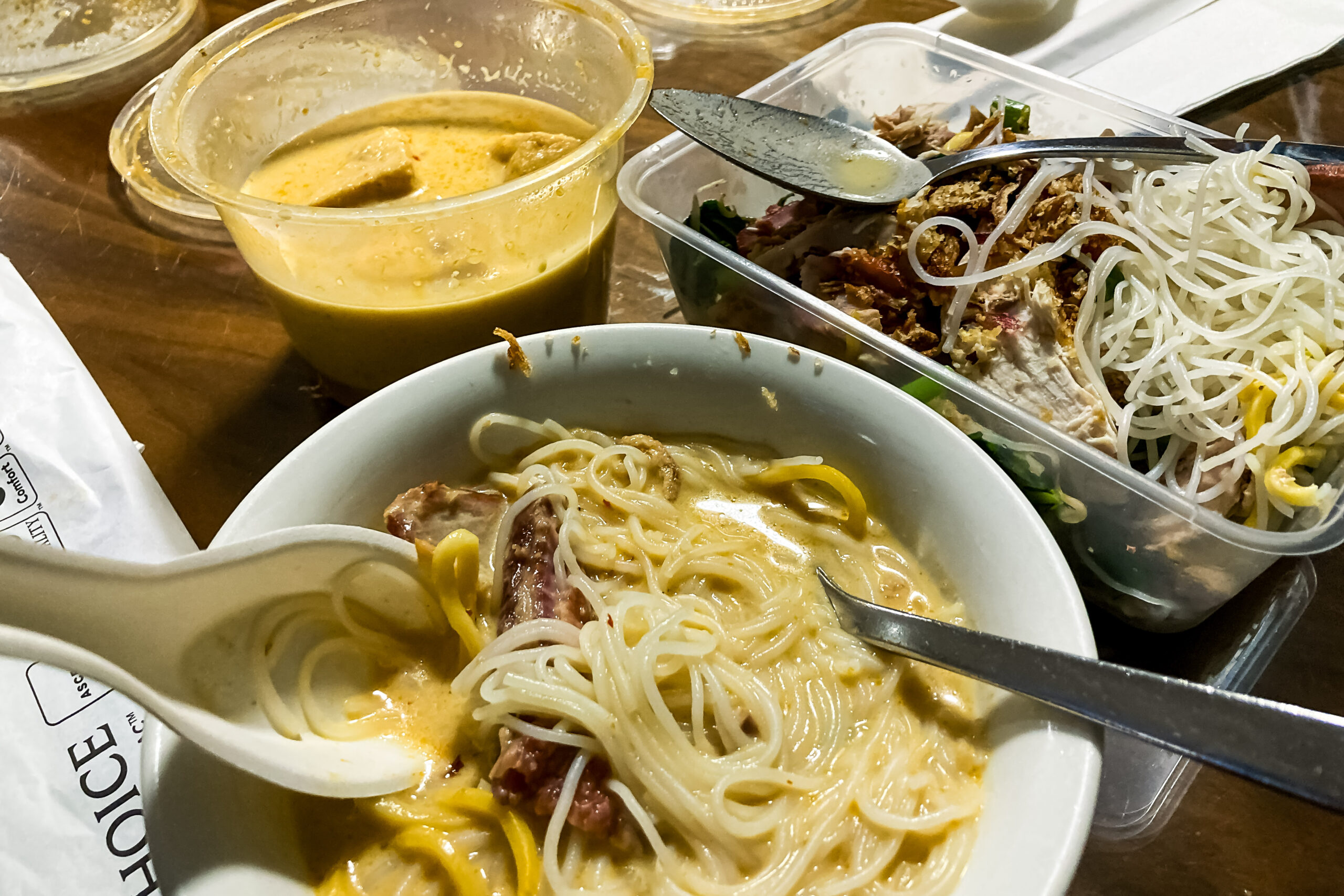 A bowl filled with noodles, and a round container with orange curry soup and an oblong container with more noodles and cooked meat