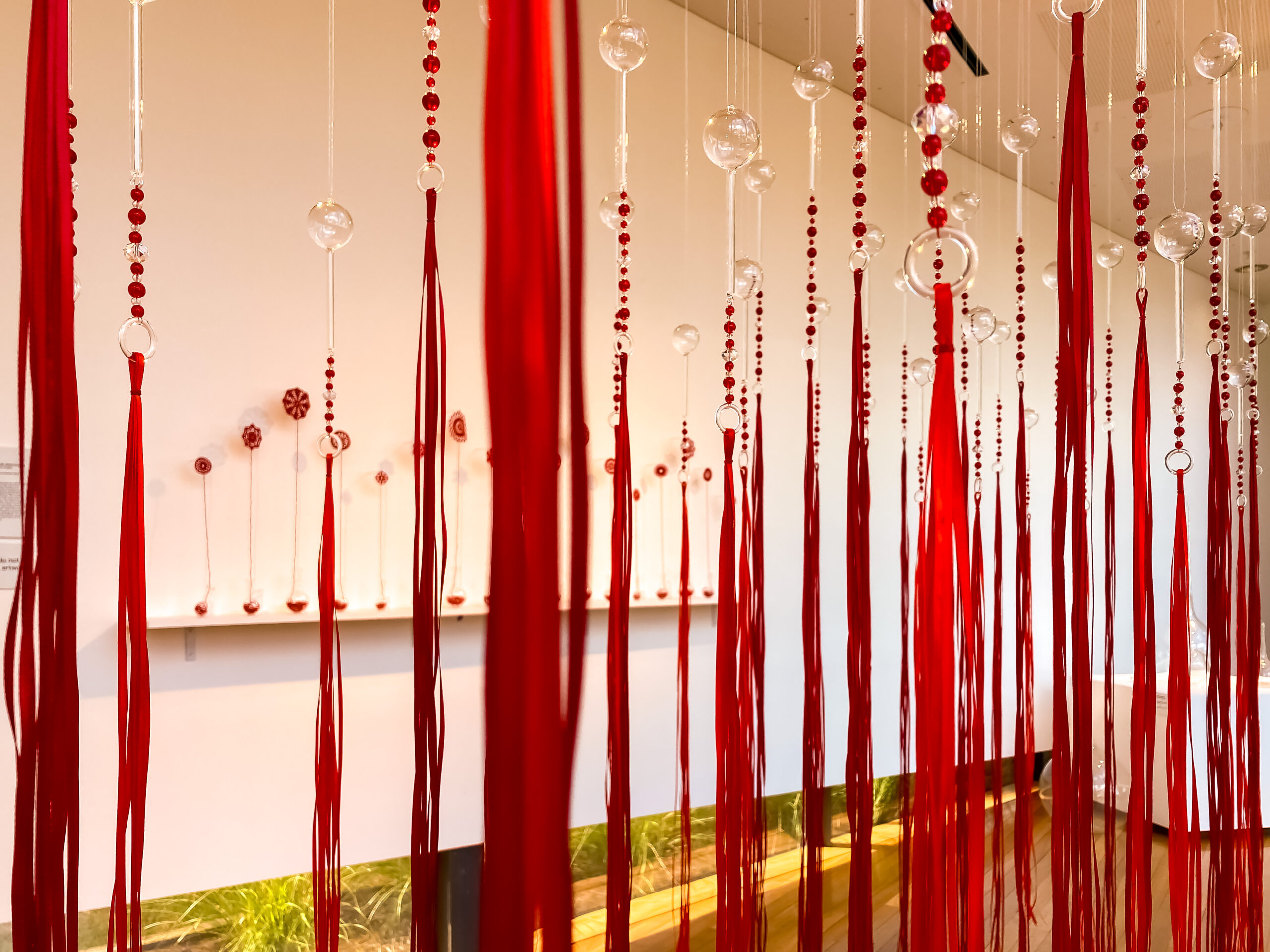Long red stands of red ribbons topped with red and clear beads and upended clear round-bottomed flasks. These are hanging suspended kind of like a forest of satin