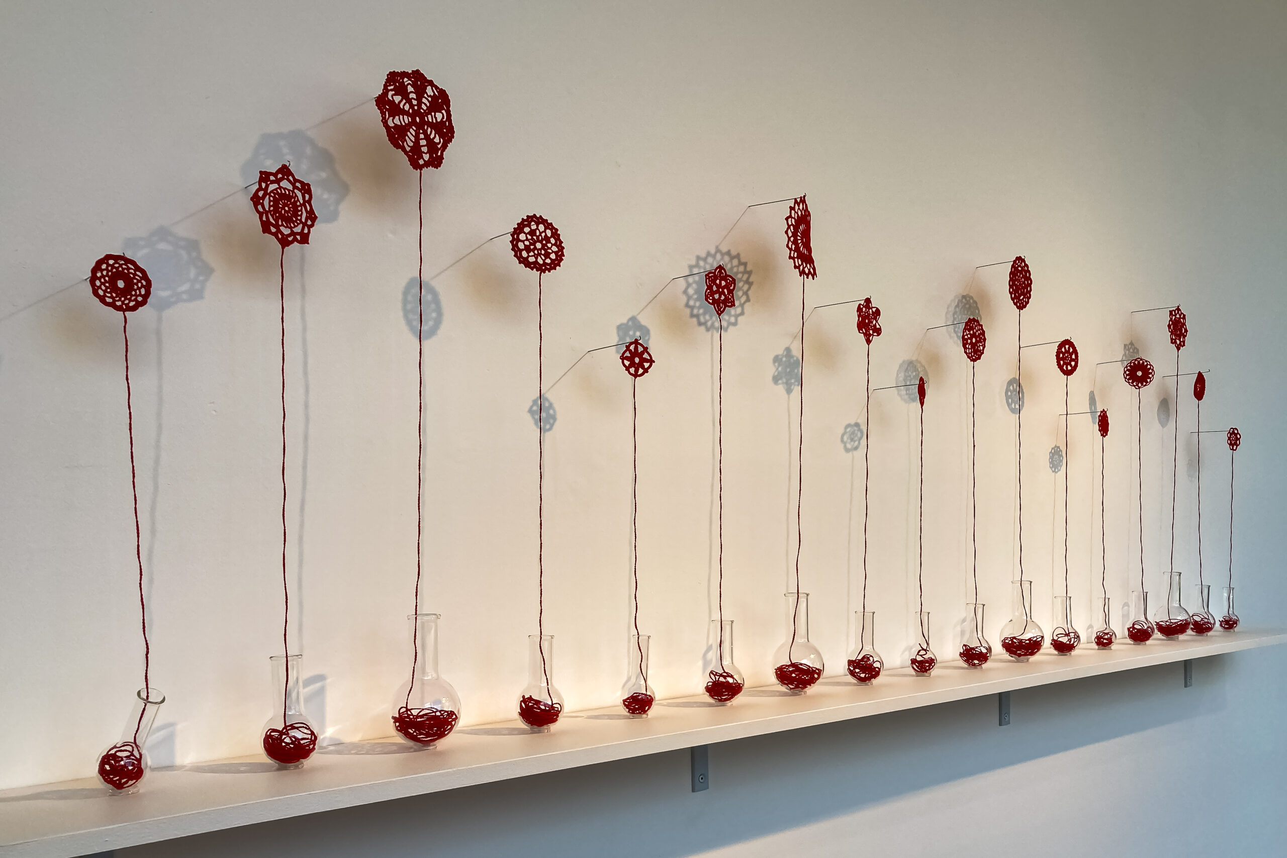 Crocheted red flowers rise from the stems of round bottomed flasks