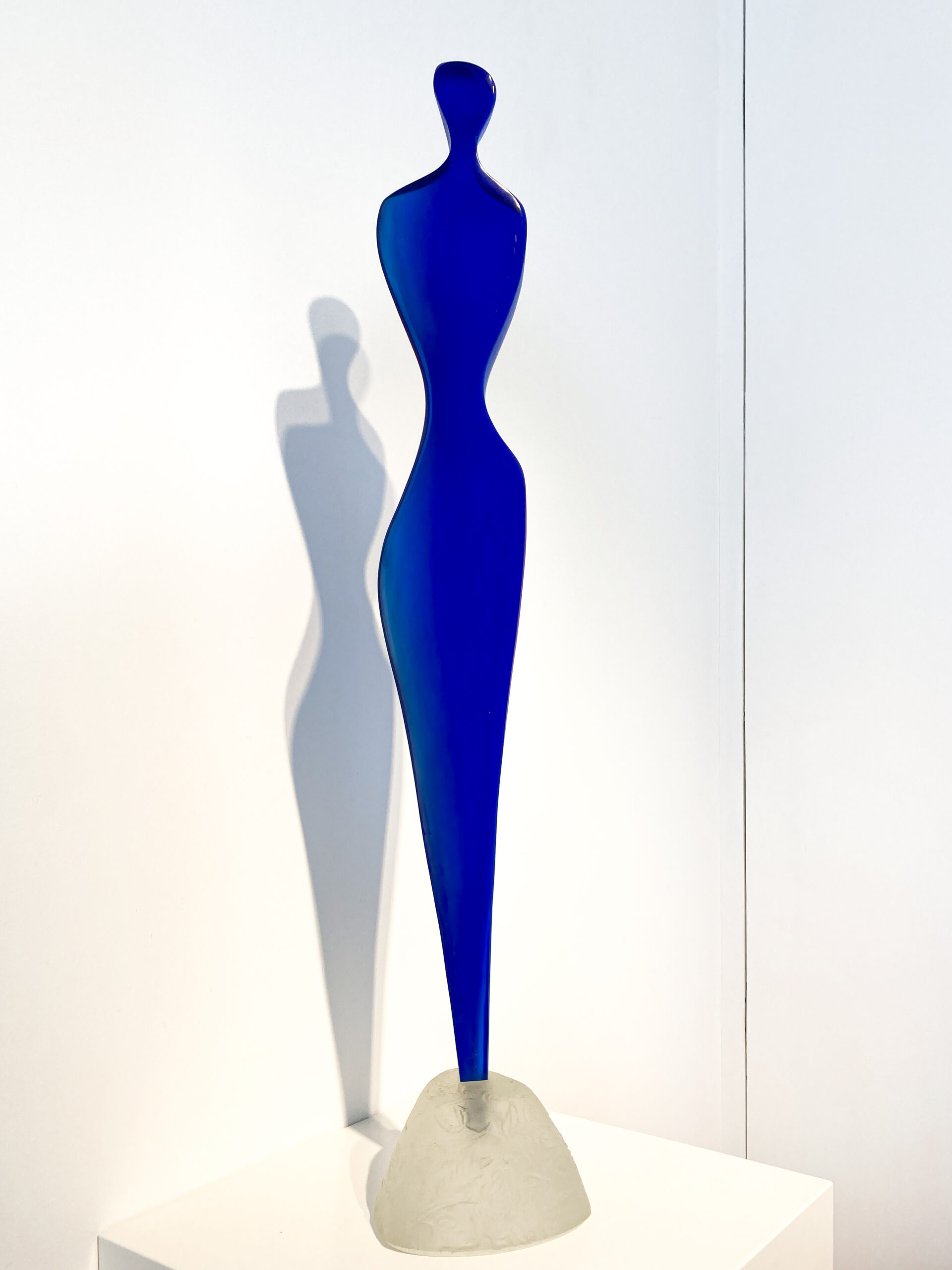A blue glass sculpture of a long curved female figure