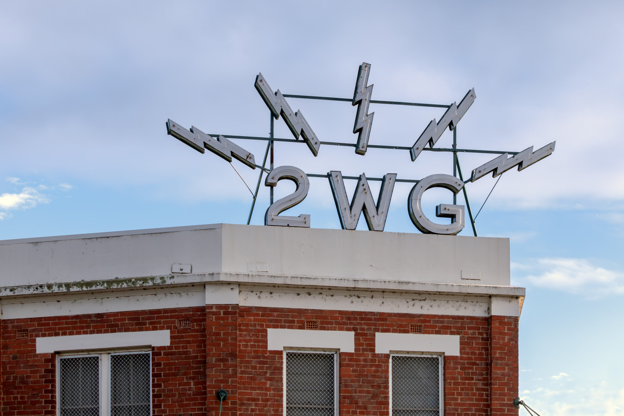 an unilluminated neon sign "2WG" with lightning strikes emanating from the letters, sits atop a red brick building