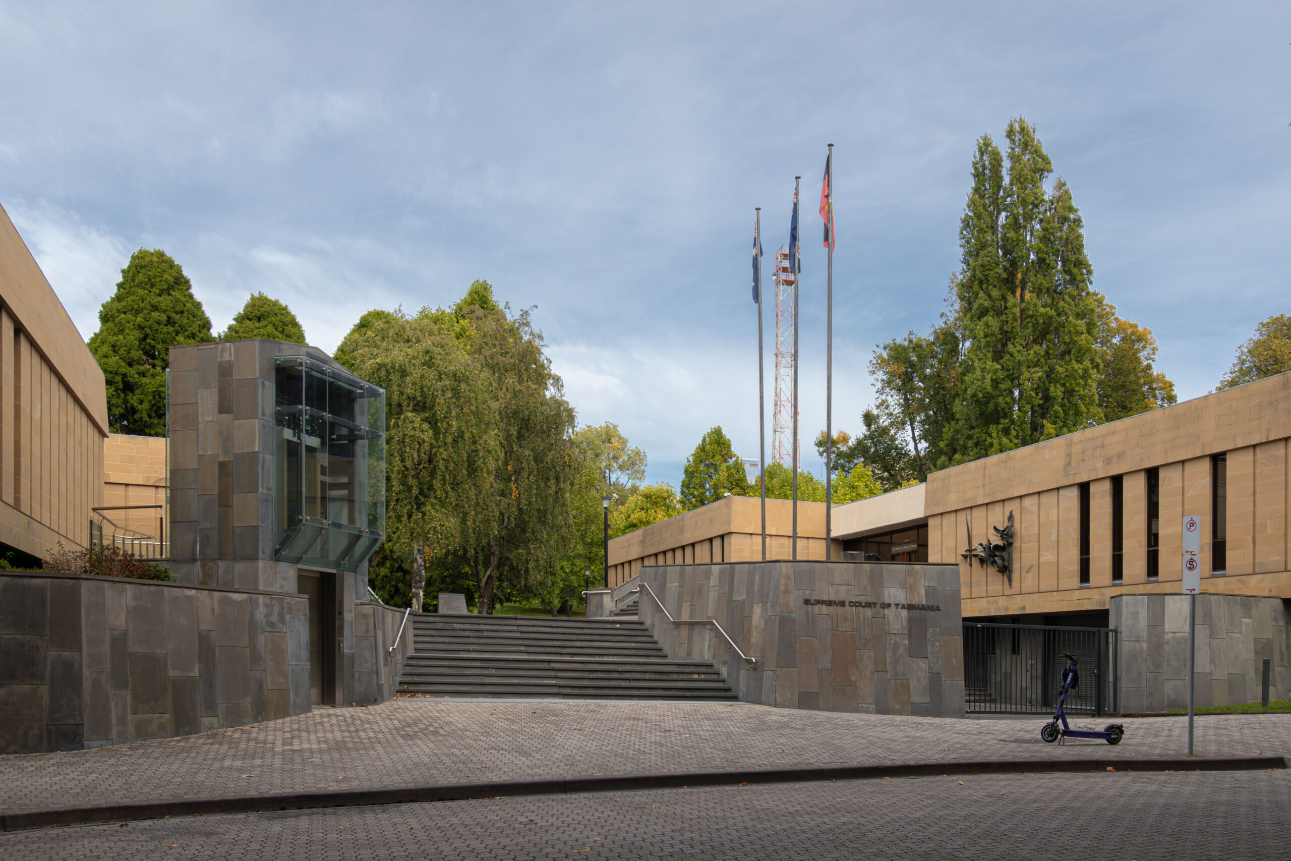 A low sandstone complex in two parts with a slate staircase in the middle and three flagpoles There is a lift to the left side