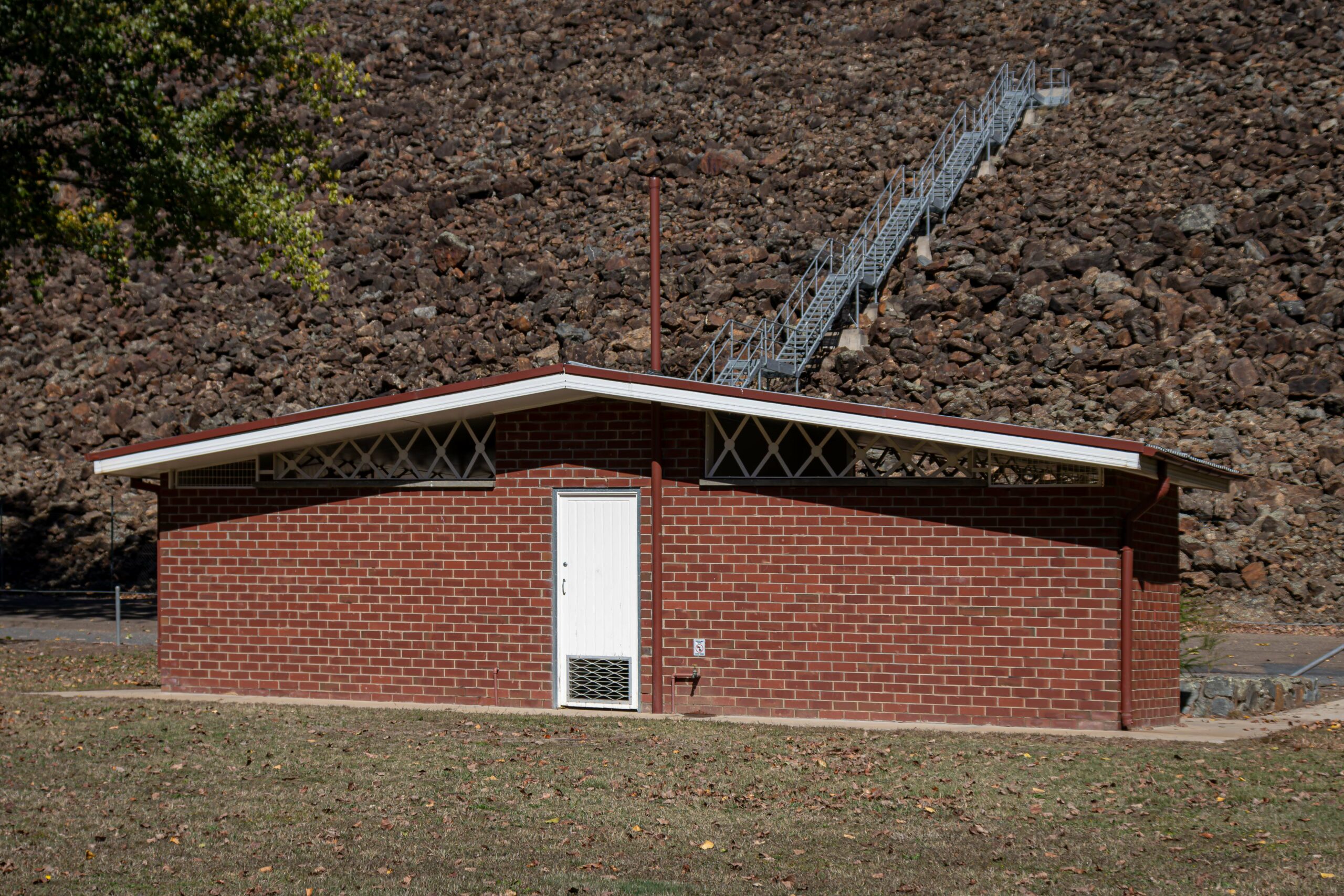 A mid-century red brick toilet block in front of a large rock wall