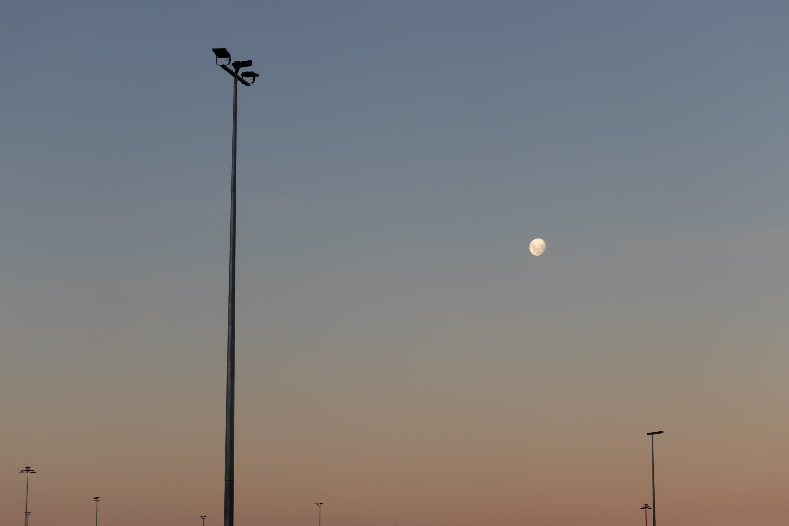 A nearly full moon in a pale dusk sky with lamp posts in the sky