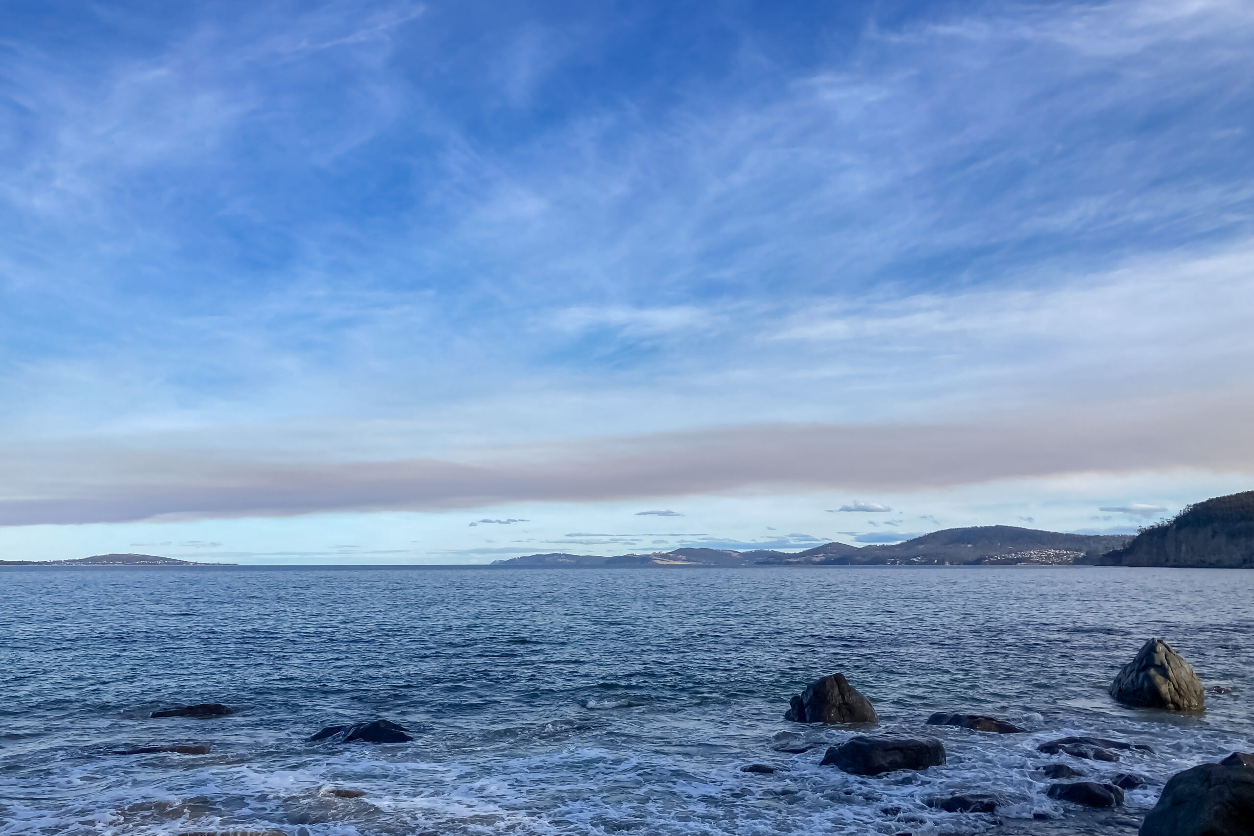 The beach with blue sky and light white clouds, and a layer of smoke haze above the water