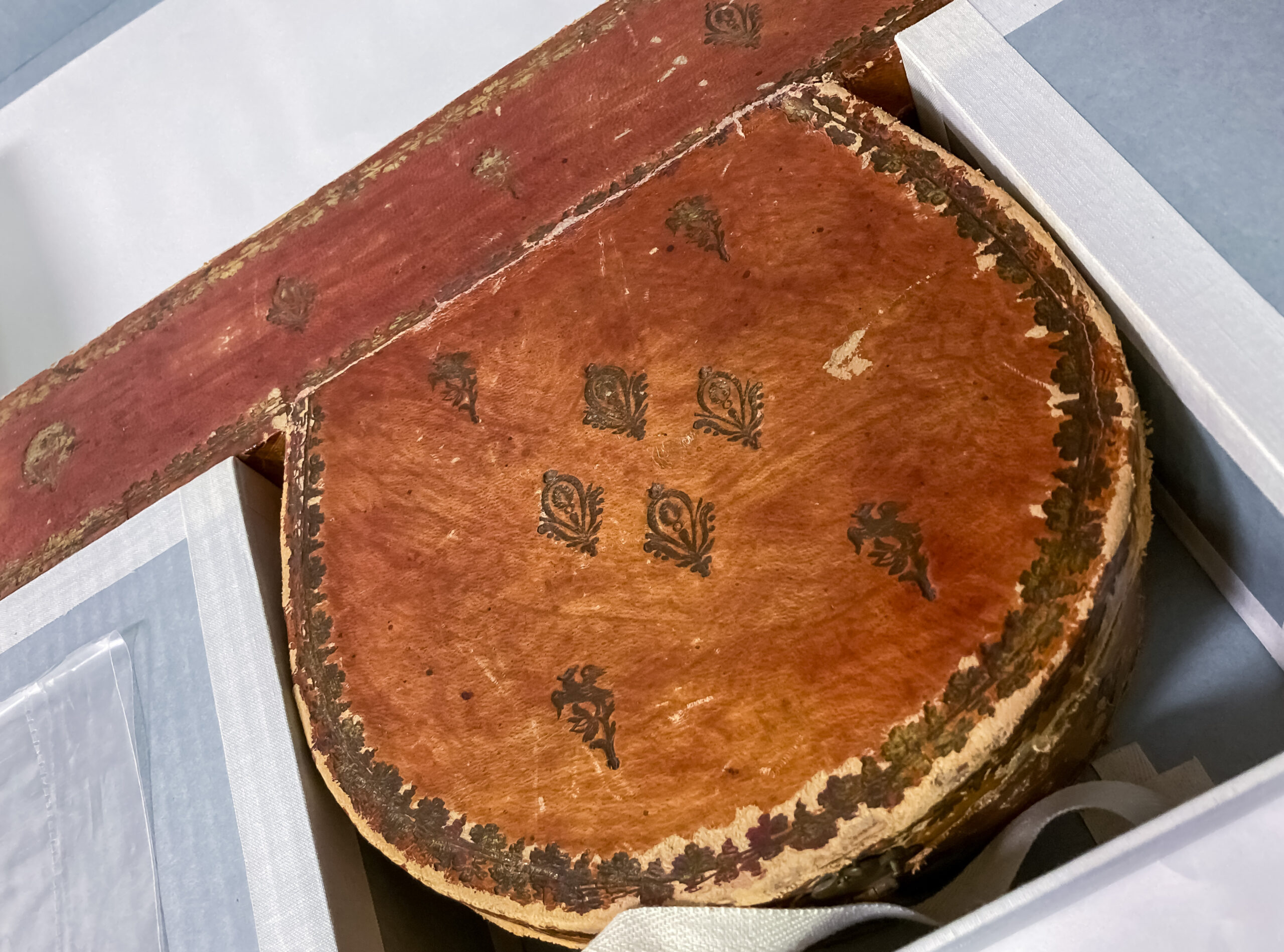 A long brown box with a round brown box attached to it with embossing on the leather