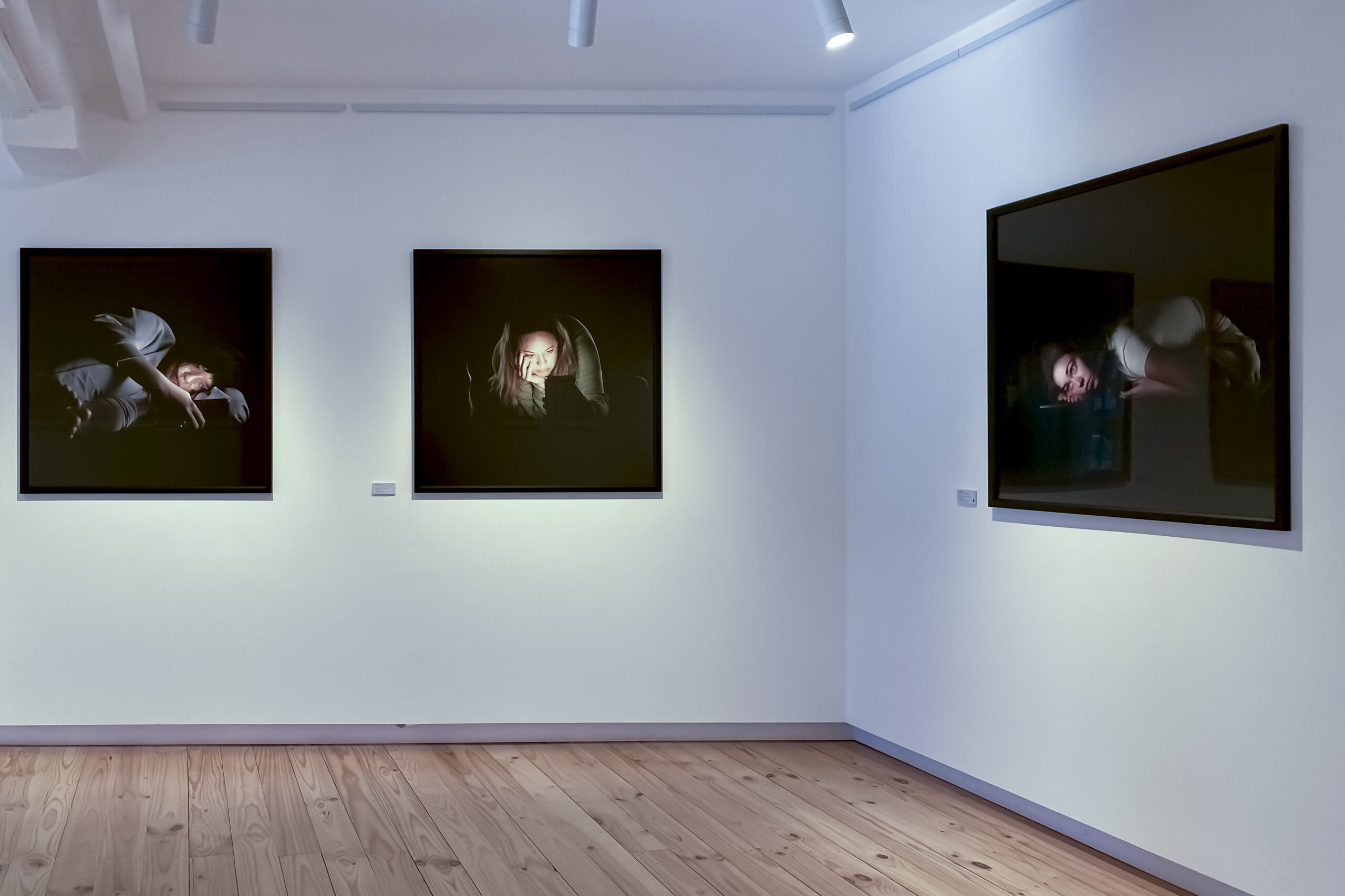Three large photographs on a white wall. The photographs depict people illuminated only by the light from their phones