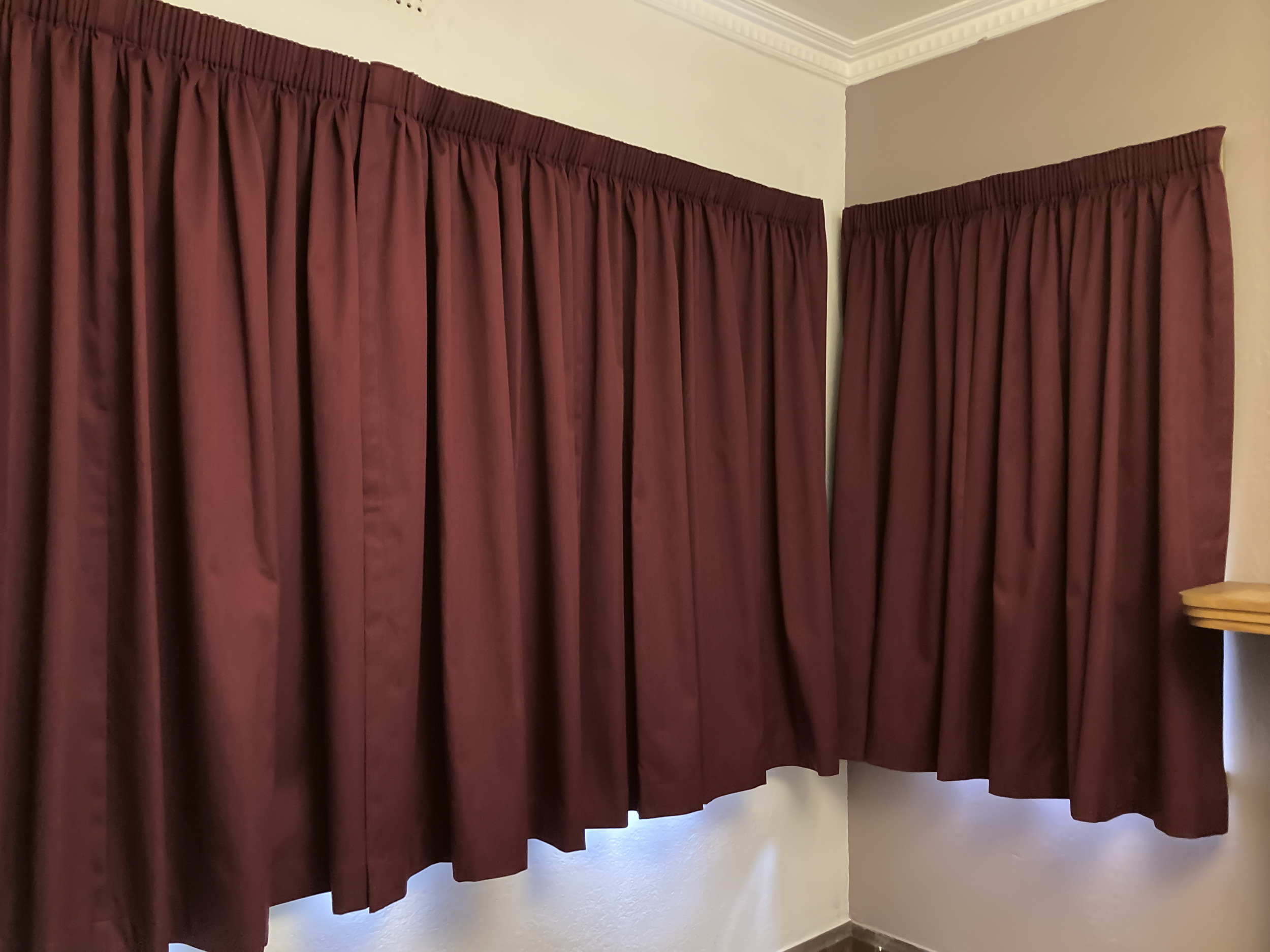 The corner of a room with a red curtain-covered window on each wall