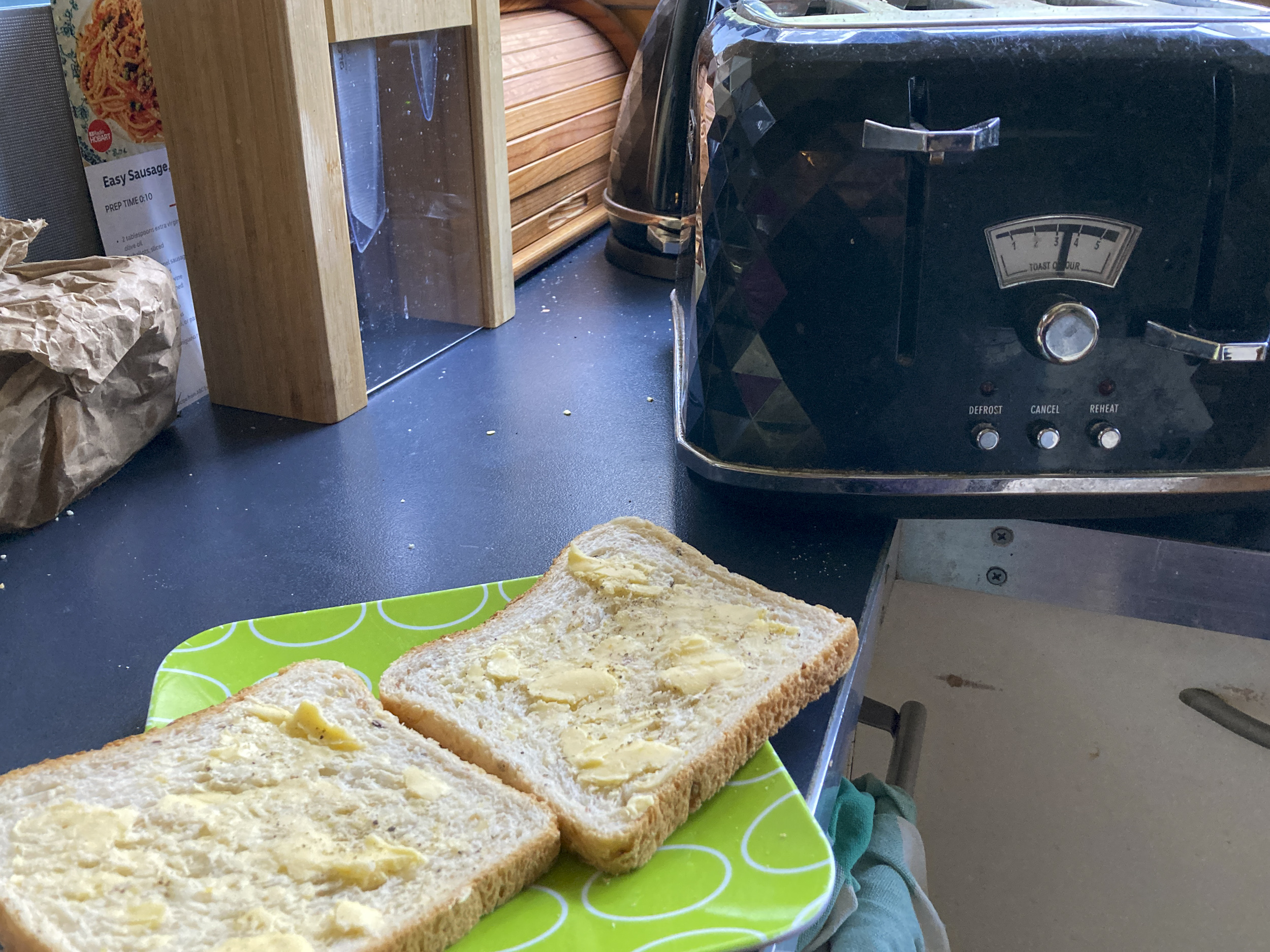 Two slices of buttered wholgreain bread on a green place, next to a black toaster