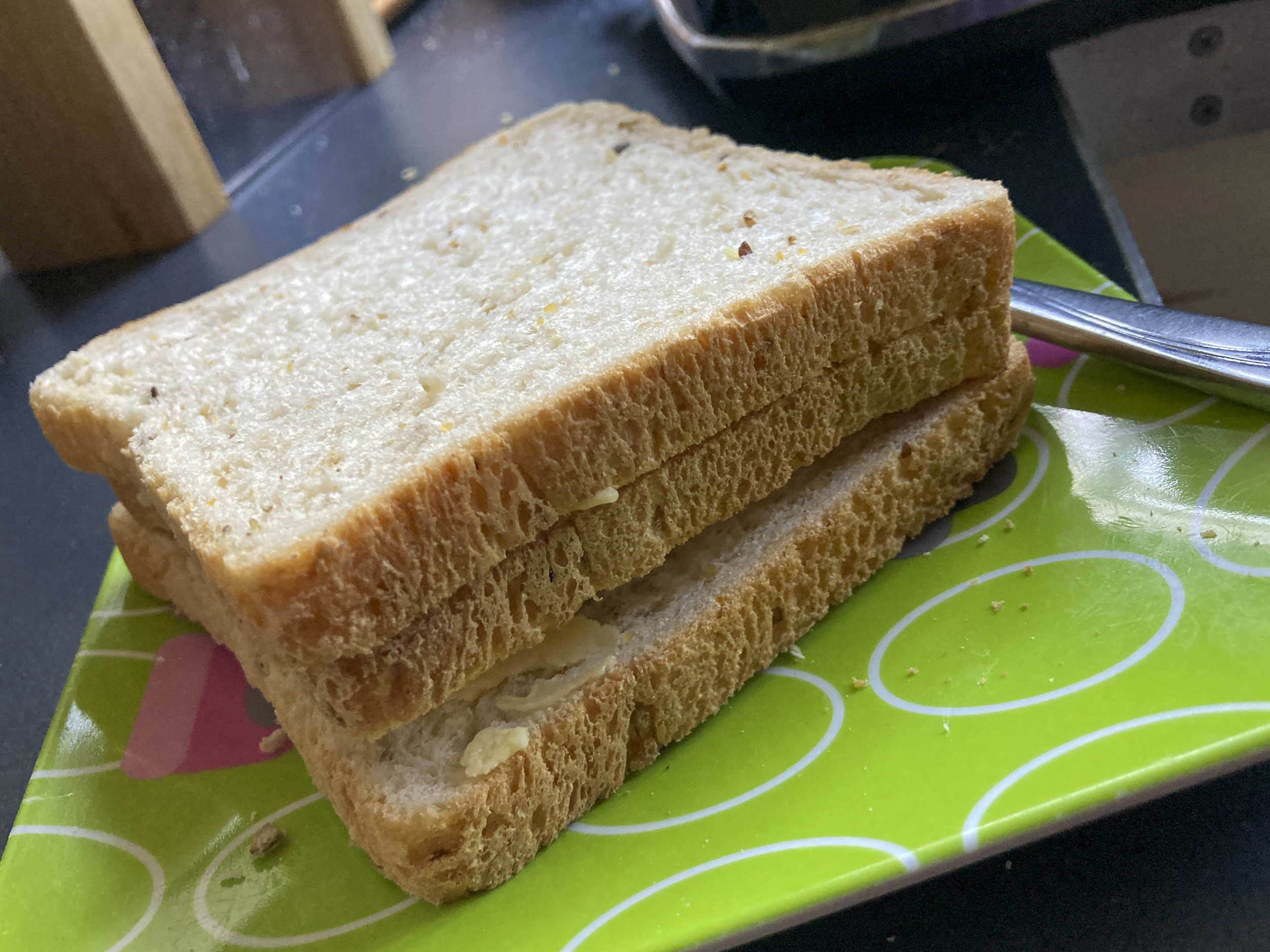 Two slices of bread with a toast between them make up a 'toast sandwich'. It is resting on a square green plate.