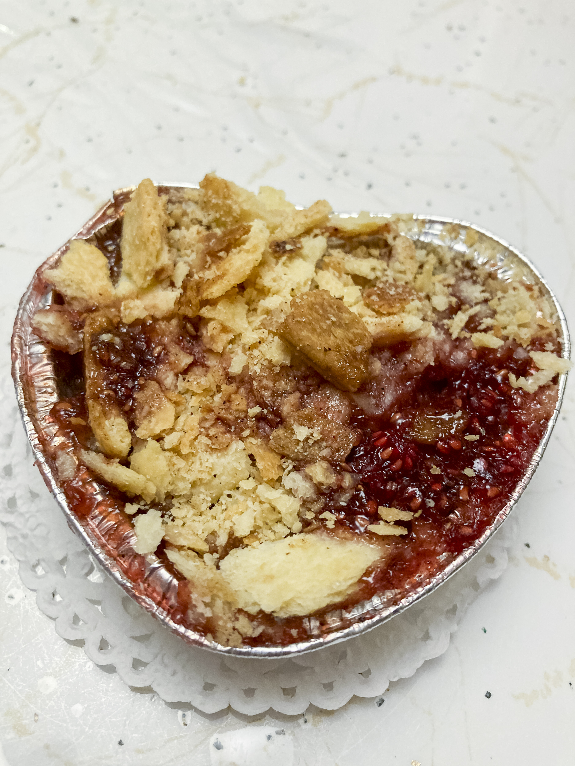 A red dessert in a heart-shaped foil tin topped with crumble