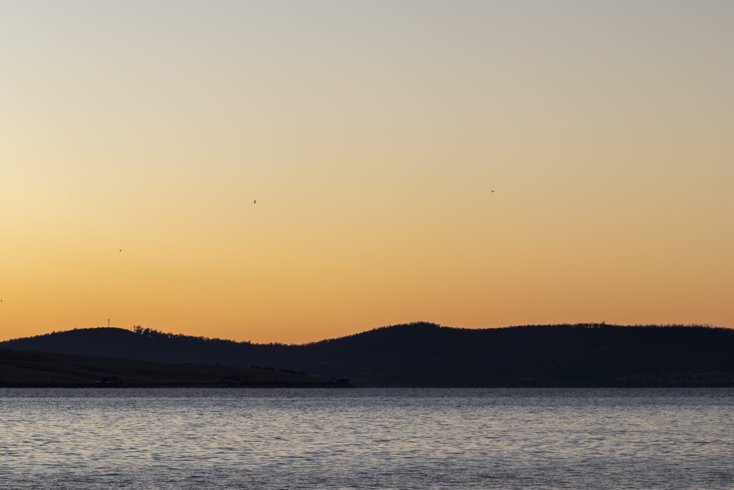 A pale orange sky over the river and hills at sunrise