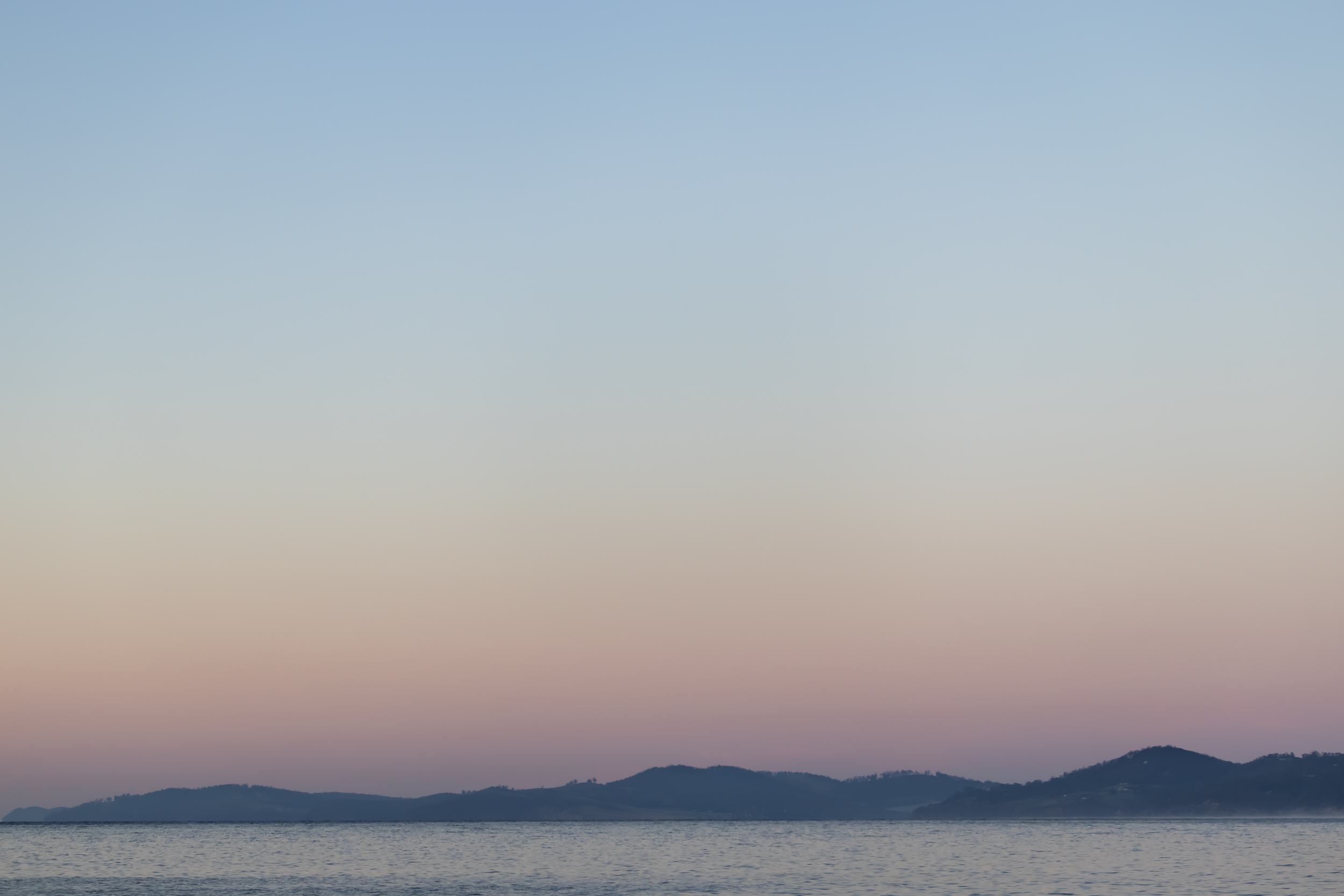 Pale sky over the river, there are layers of pastel blue, yellow and orange