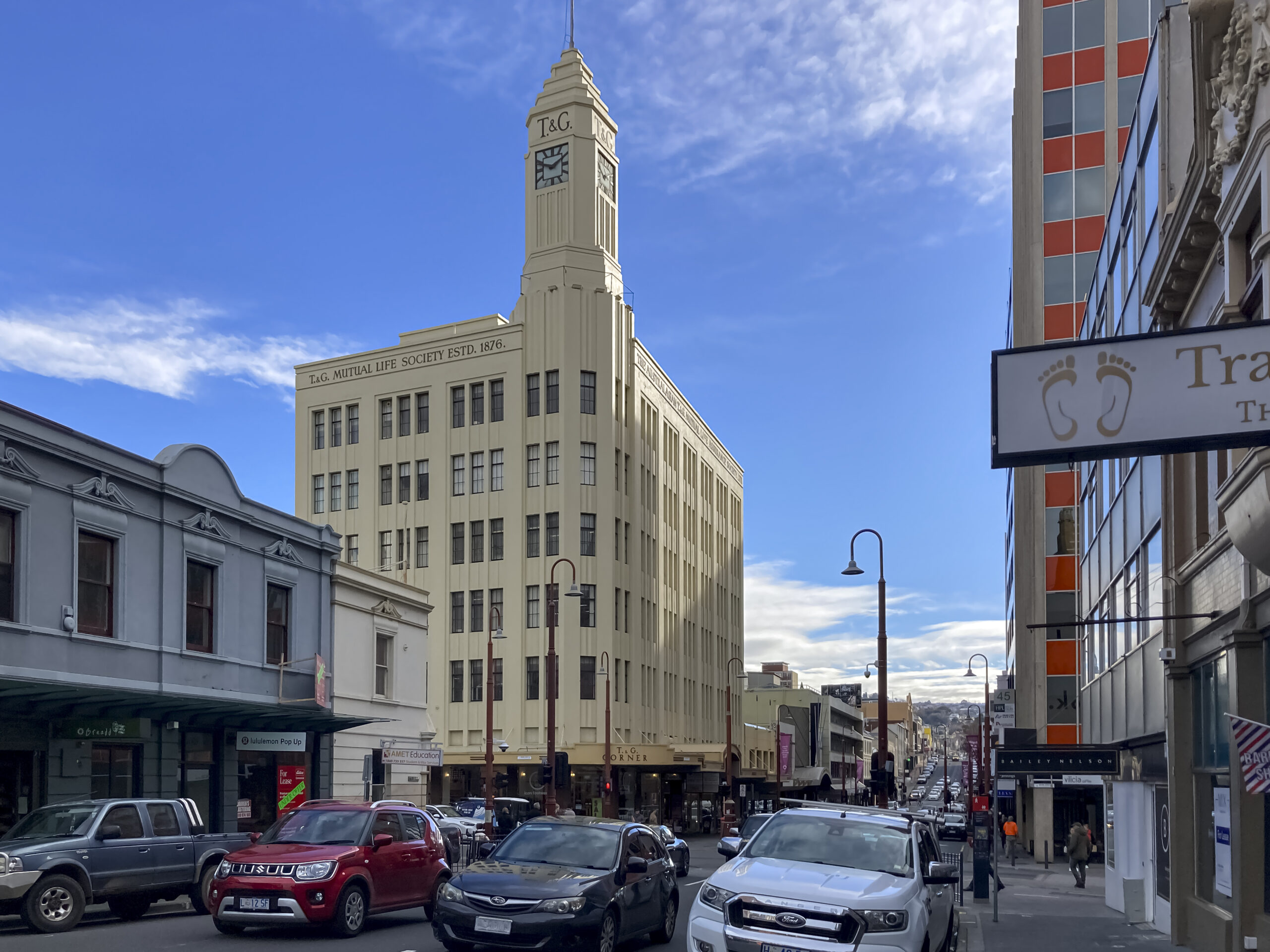 A street view with a 5-storey art deco building featuring prominently. It has a high clock tower. 