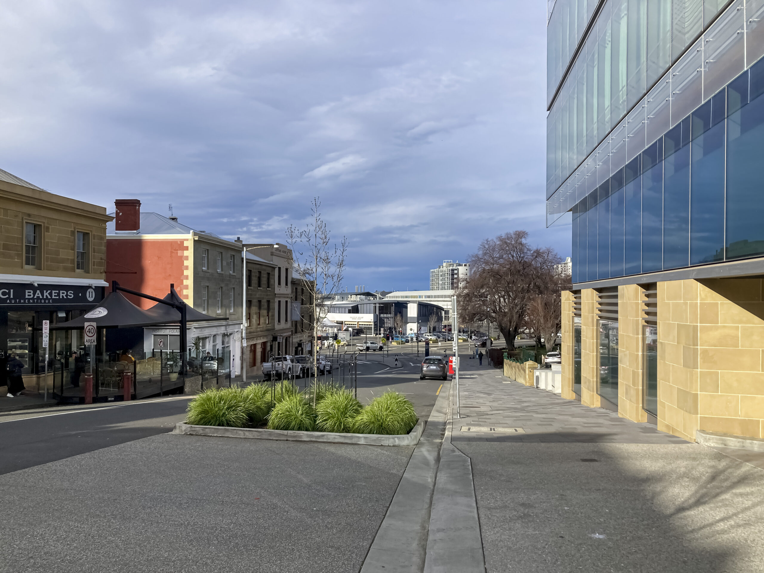 A streetscape with grey skies. There is a large glass building on the right hand side