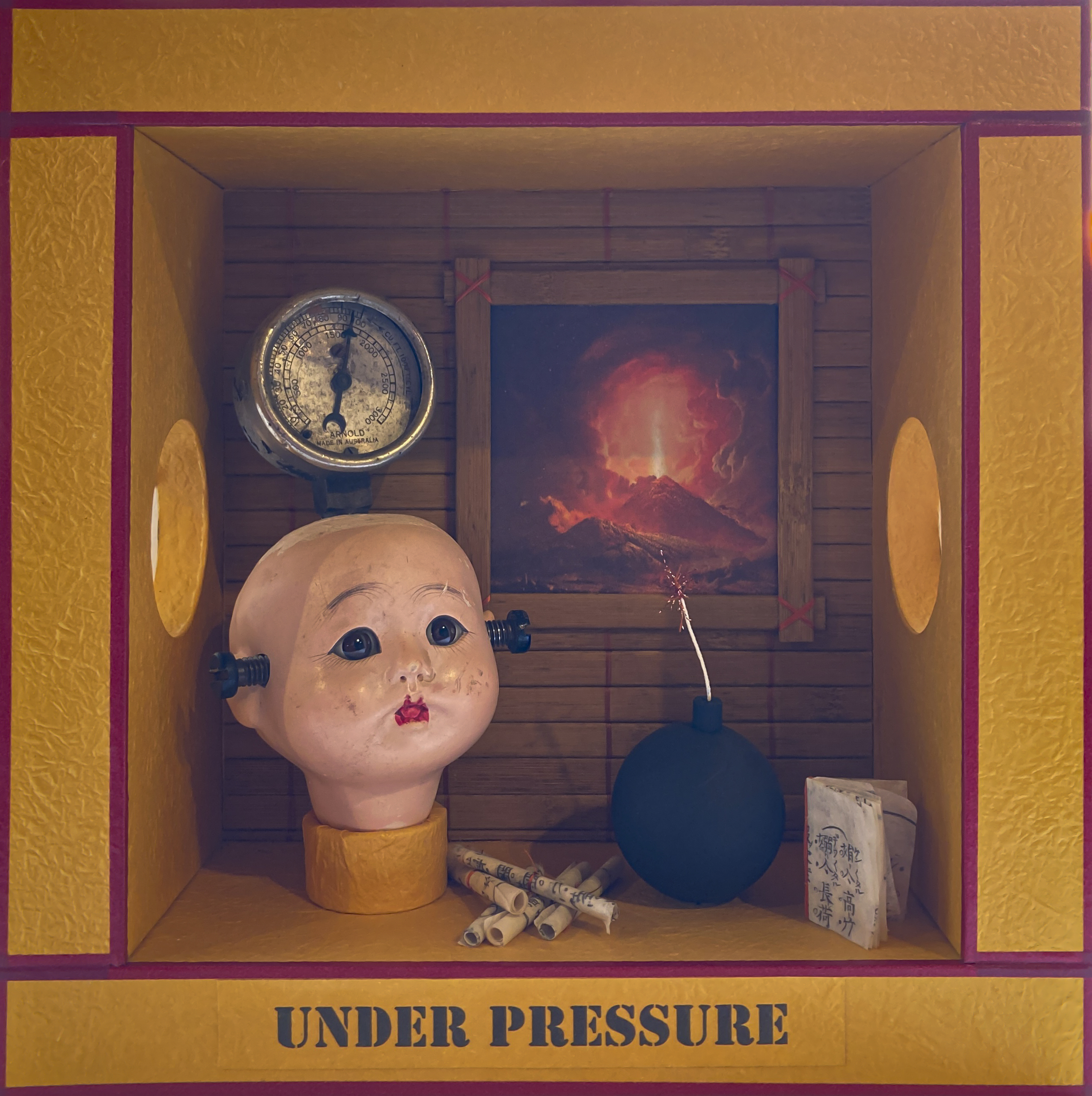 A diorama in a box titled Under Pressure, with elements including a doll's head, a timer and abomb