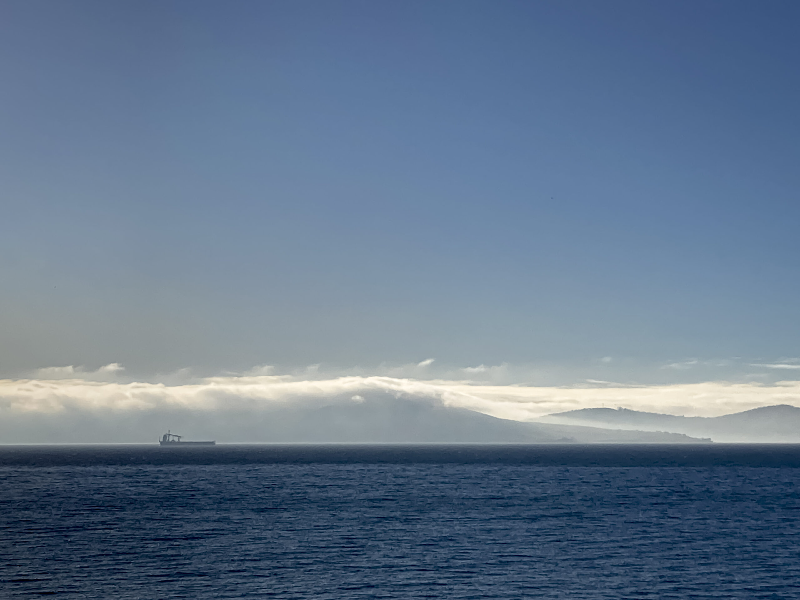 A layer of fog over the river, with blue sky above, and a boat shrouded in fog