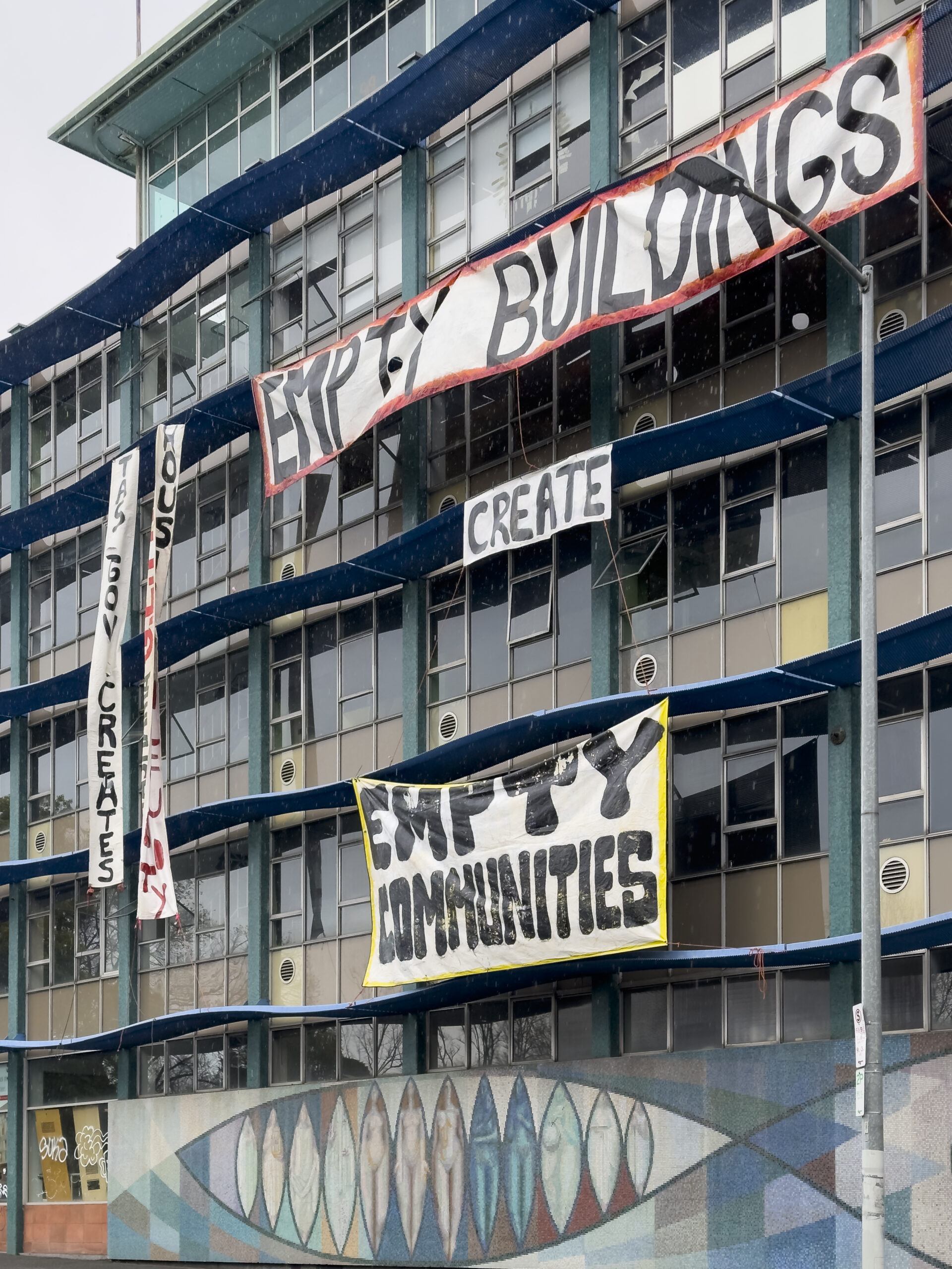 Banners hanging from a five-storey glass curtain wall building proclaiming "Empty buildings create empty communities"