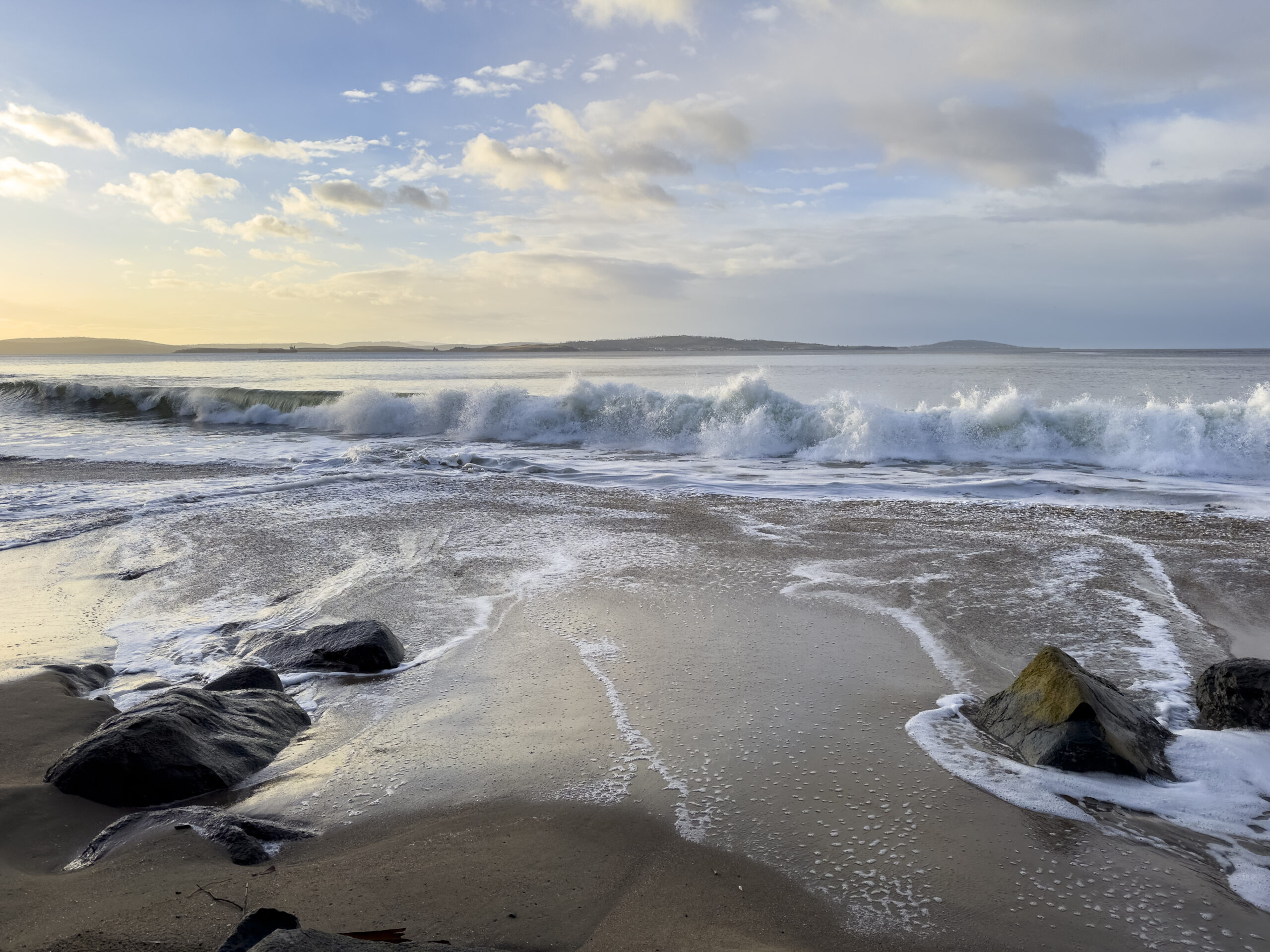 A low wave coming in to an empty beach with blue cloudy sky in the background