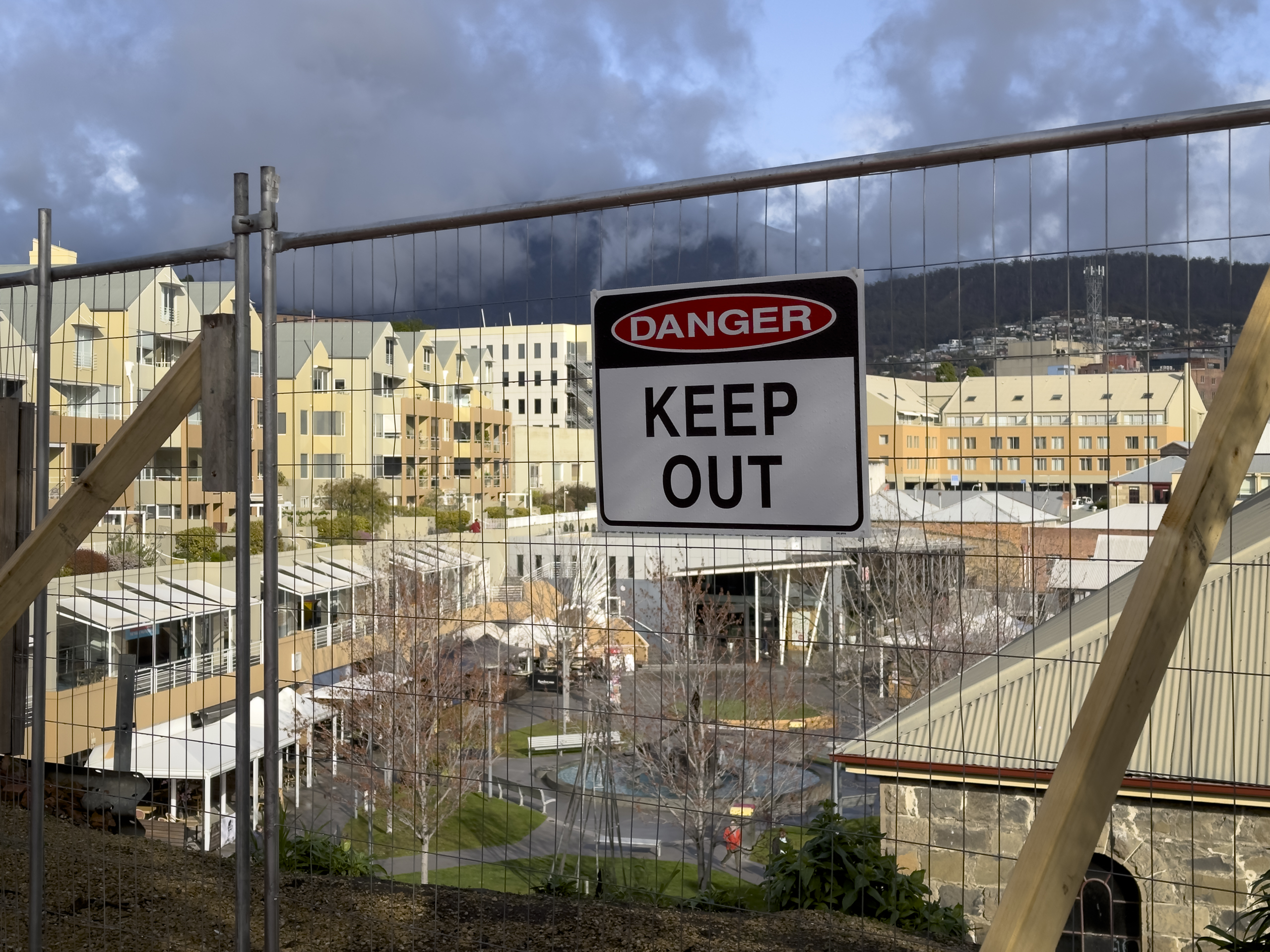 A construction fence with a 'keep out' sign high above a courtyard surrounded by modern buildings