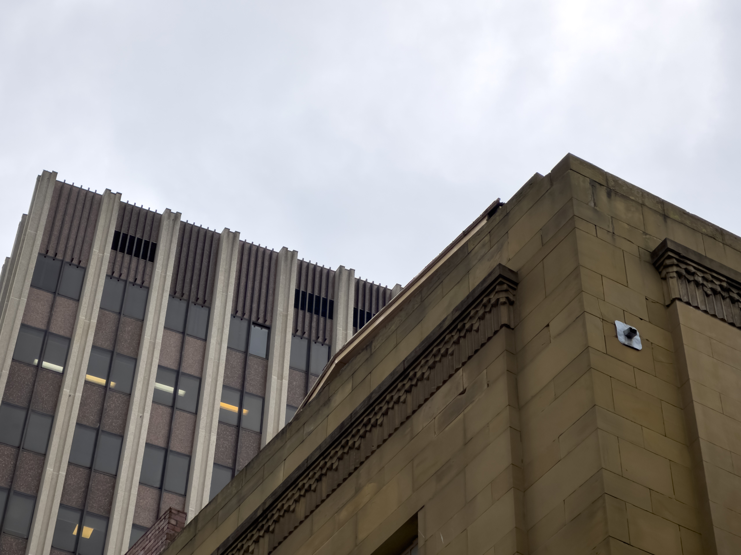 Corner of a blocky sandstone building in front of a much higher concrete 