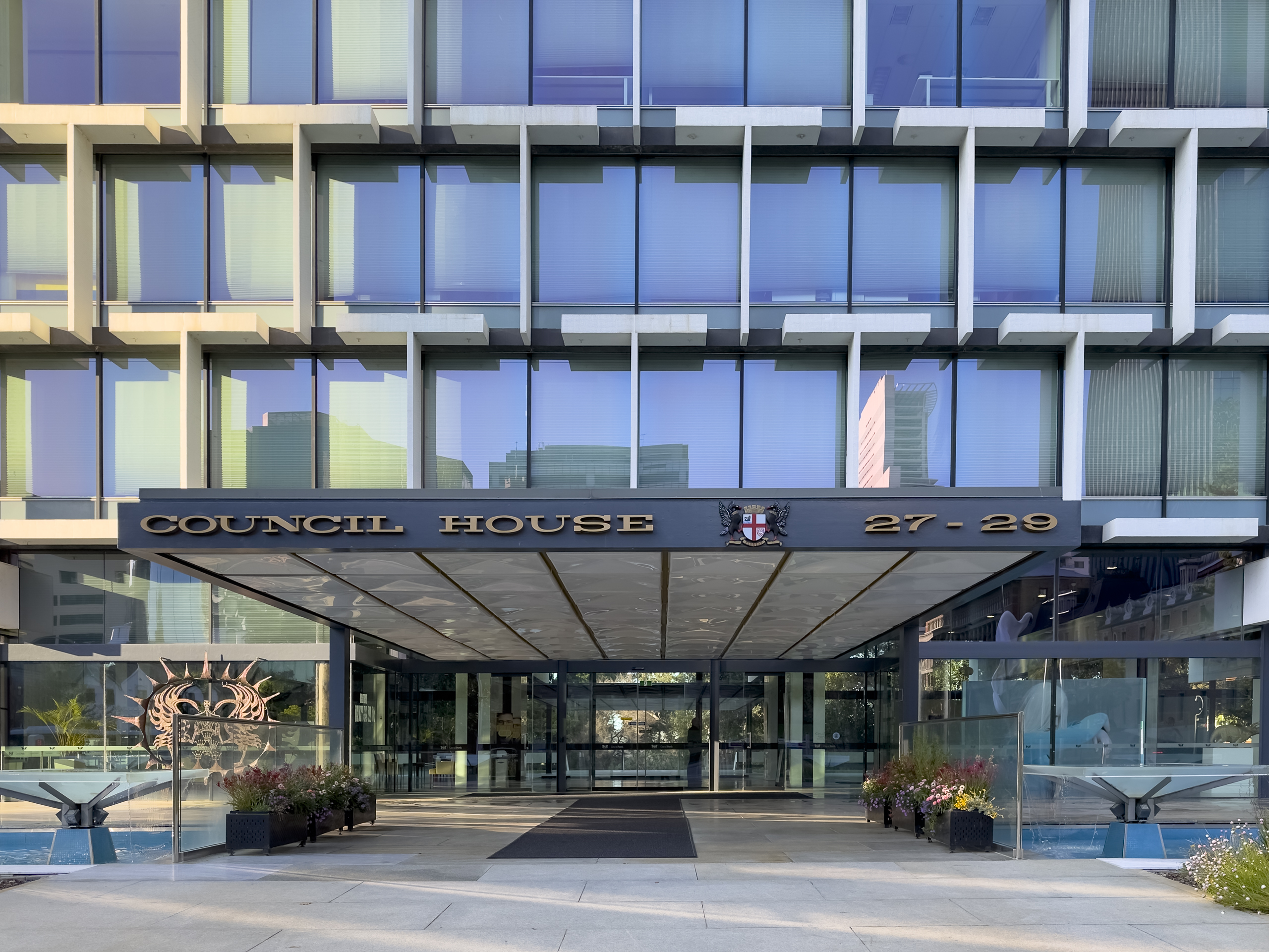 A close-in photo of a glass curtain facade; The words "Council House 27-29" are on the entrance verandah