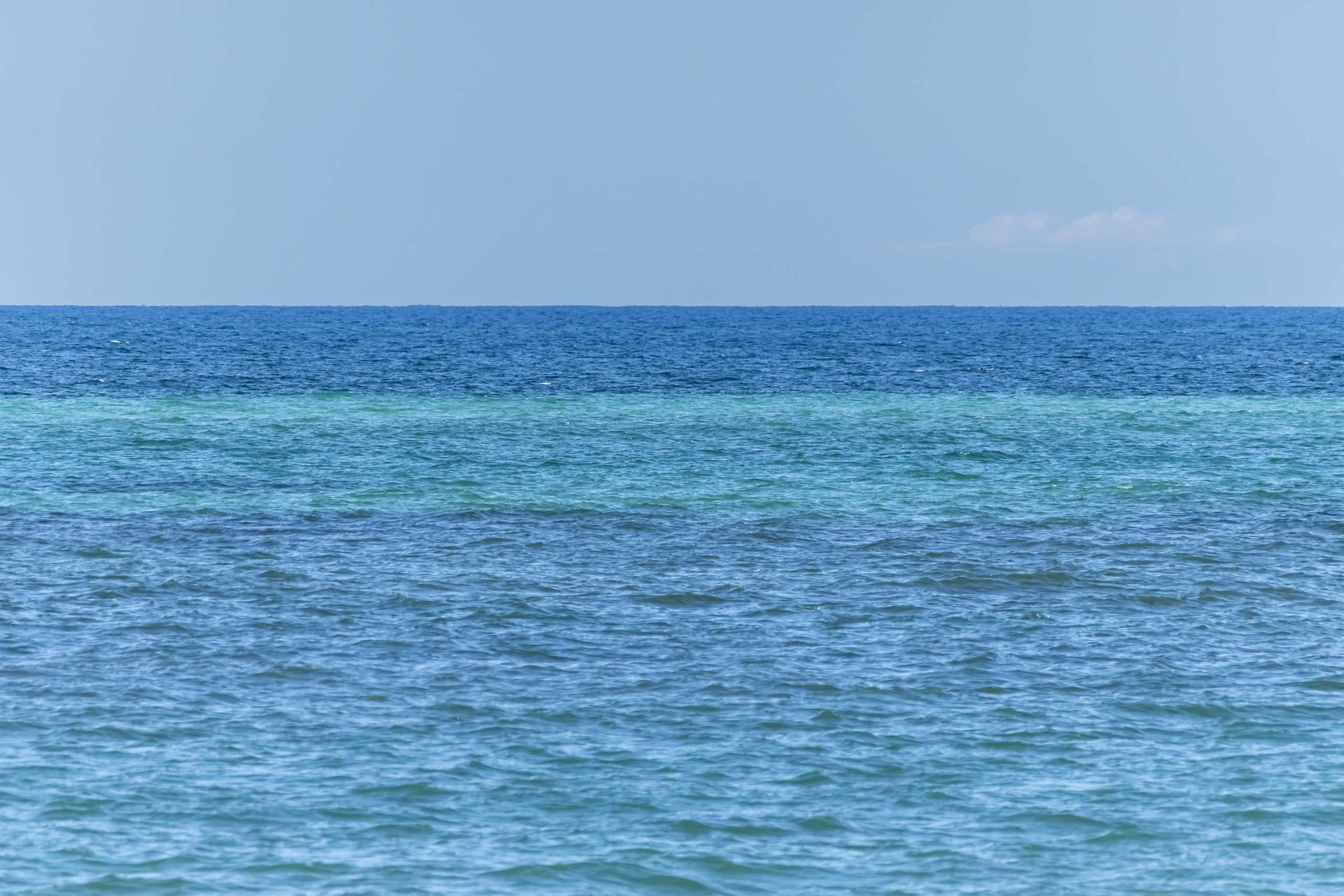 Layers of different shades of blue water against a blue sky