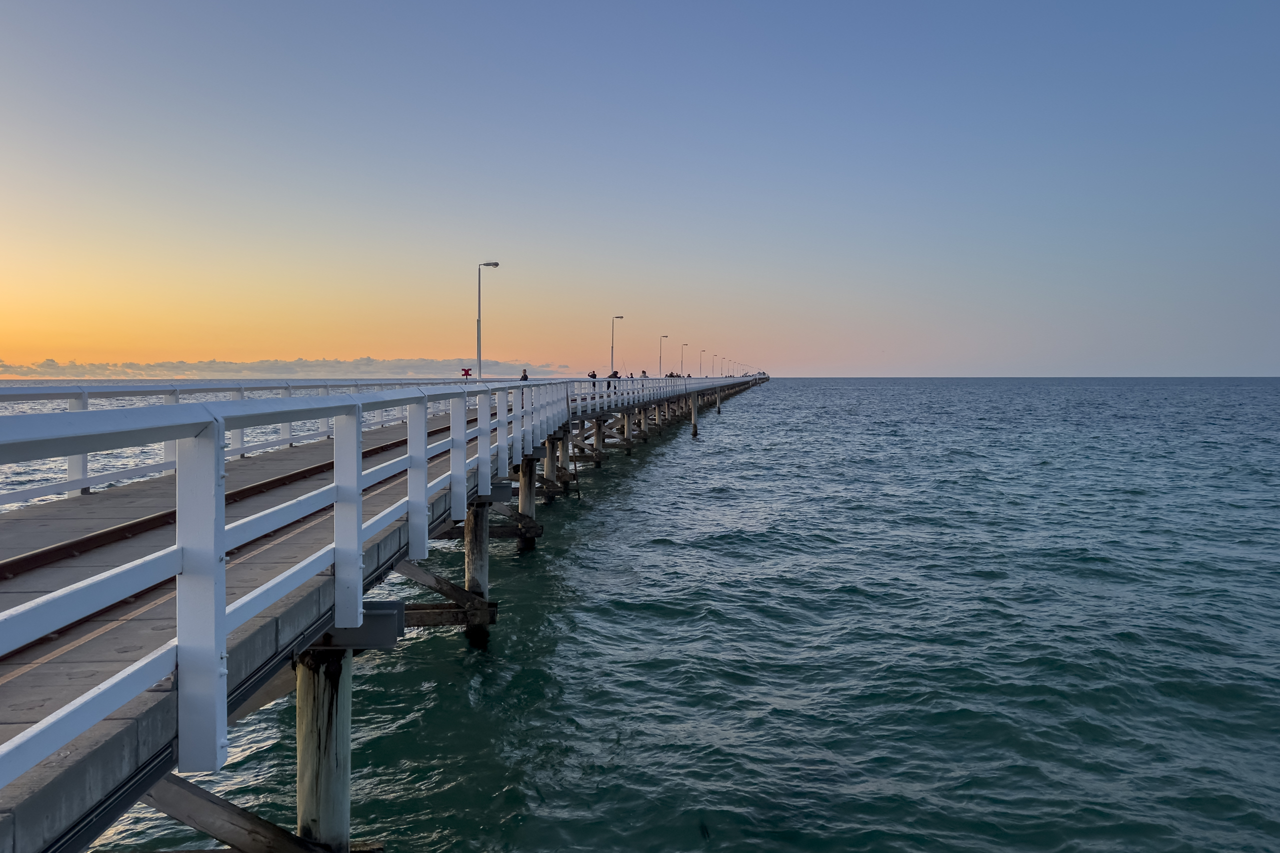 A long timber jetty stretching out to sea at sunset