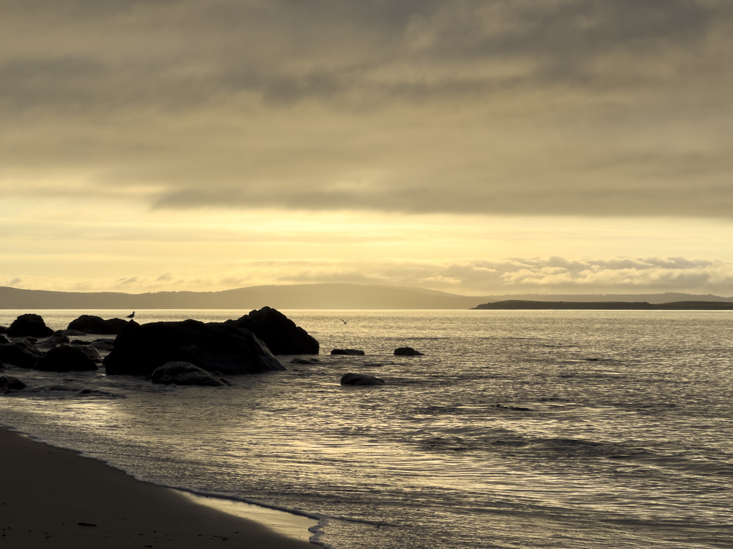 A sunrise photo of a beach. There are rocks in the midground and the colour tone is predominantly yellow