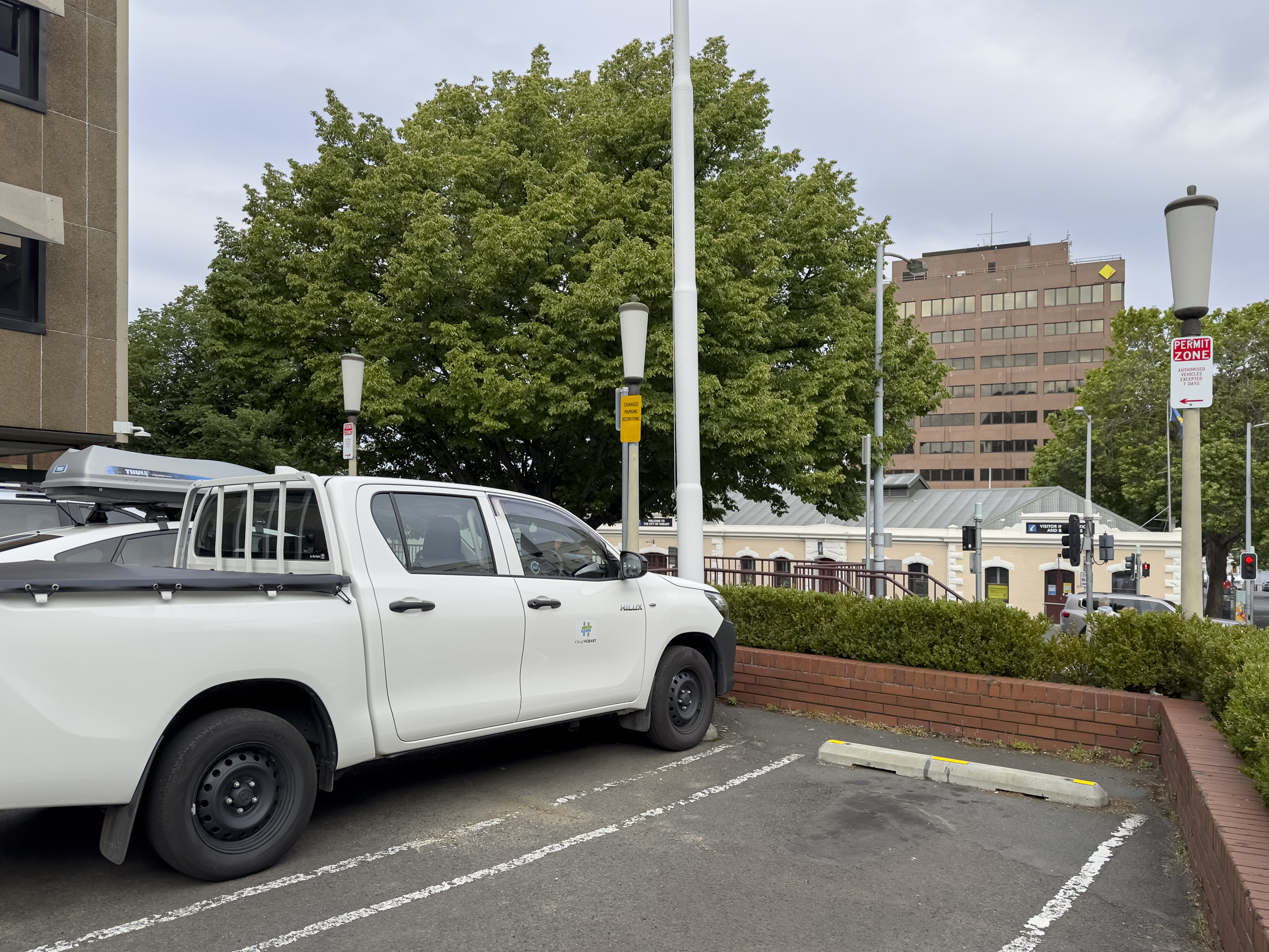 A whiite ute in a parking space, next to an empty space. A sign reads 'permit zone'