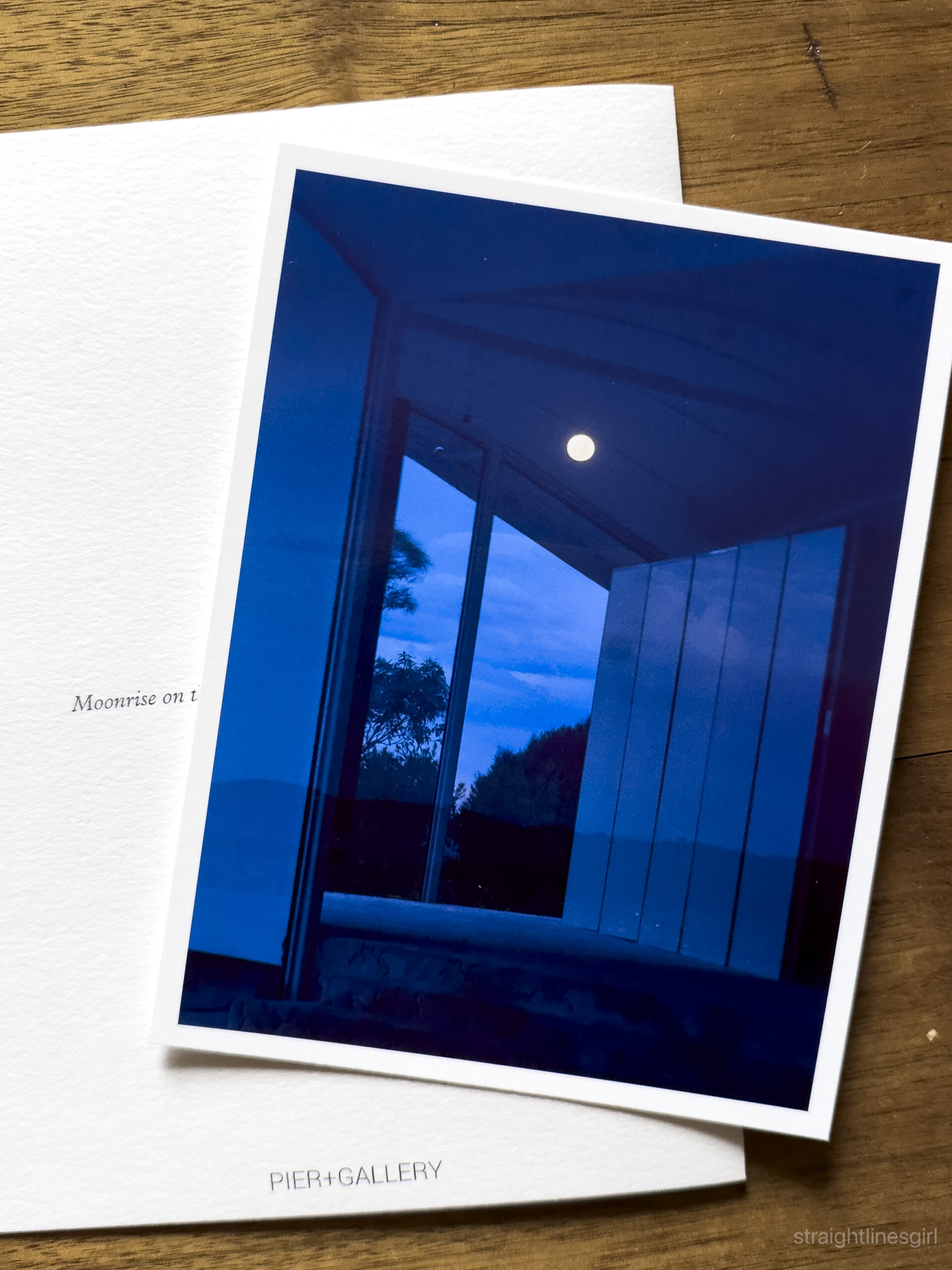 A photograph looking out of a window to a full moon over the river. The photo is different shades of blue