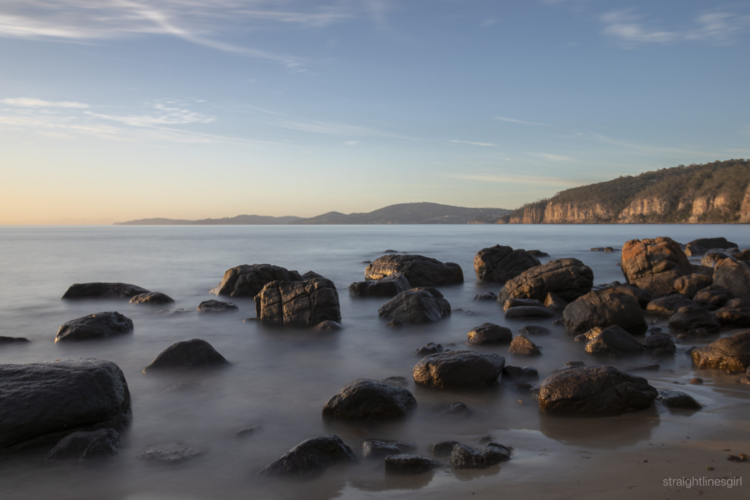 The beach early in the morning, with soft blurred water and there are rocks in the water