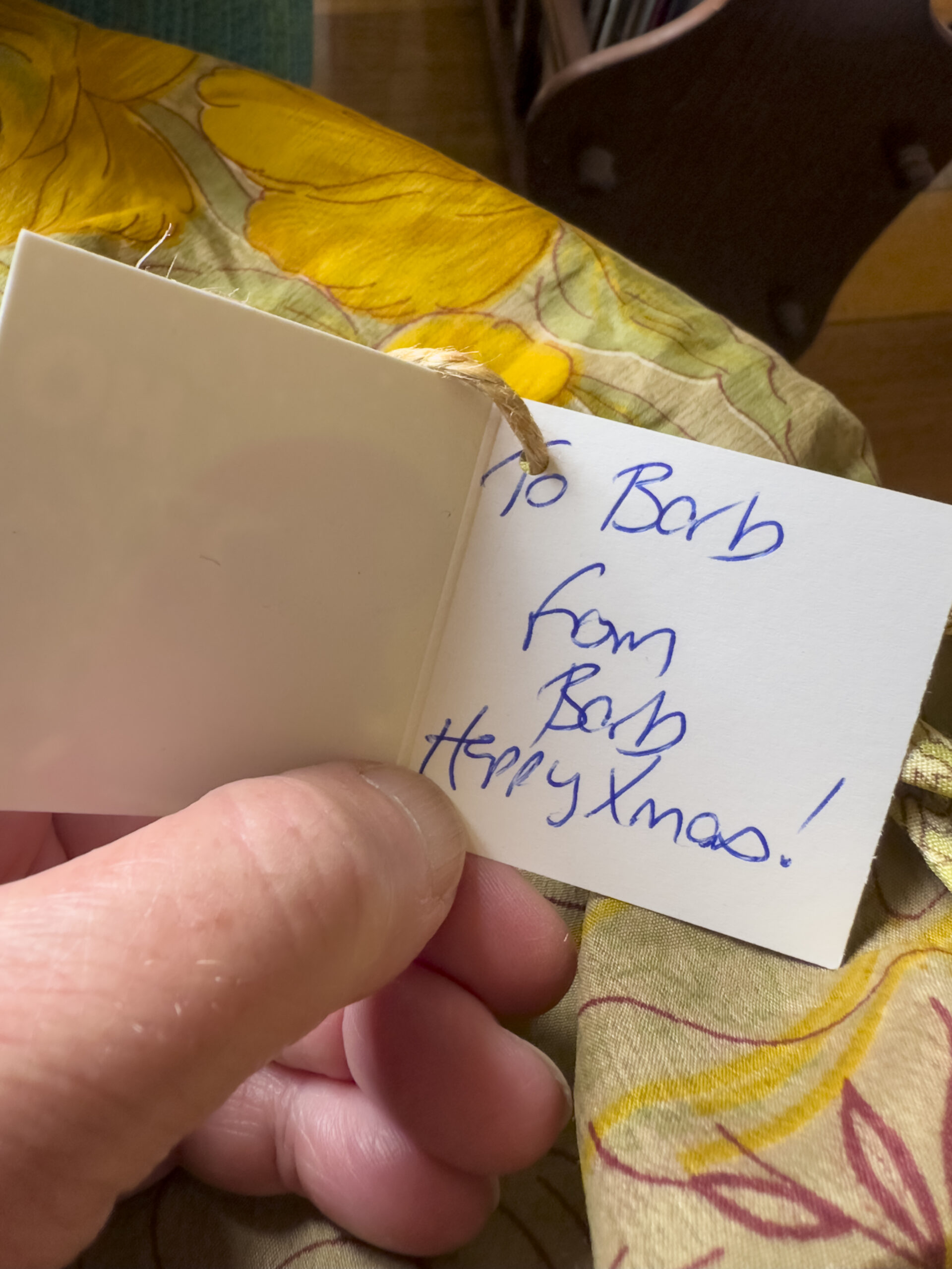 A hand holding a gift tag that says "to Barb from Barb Happy Xmas!"