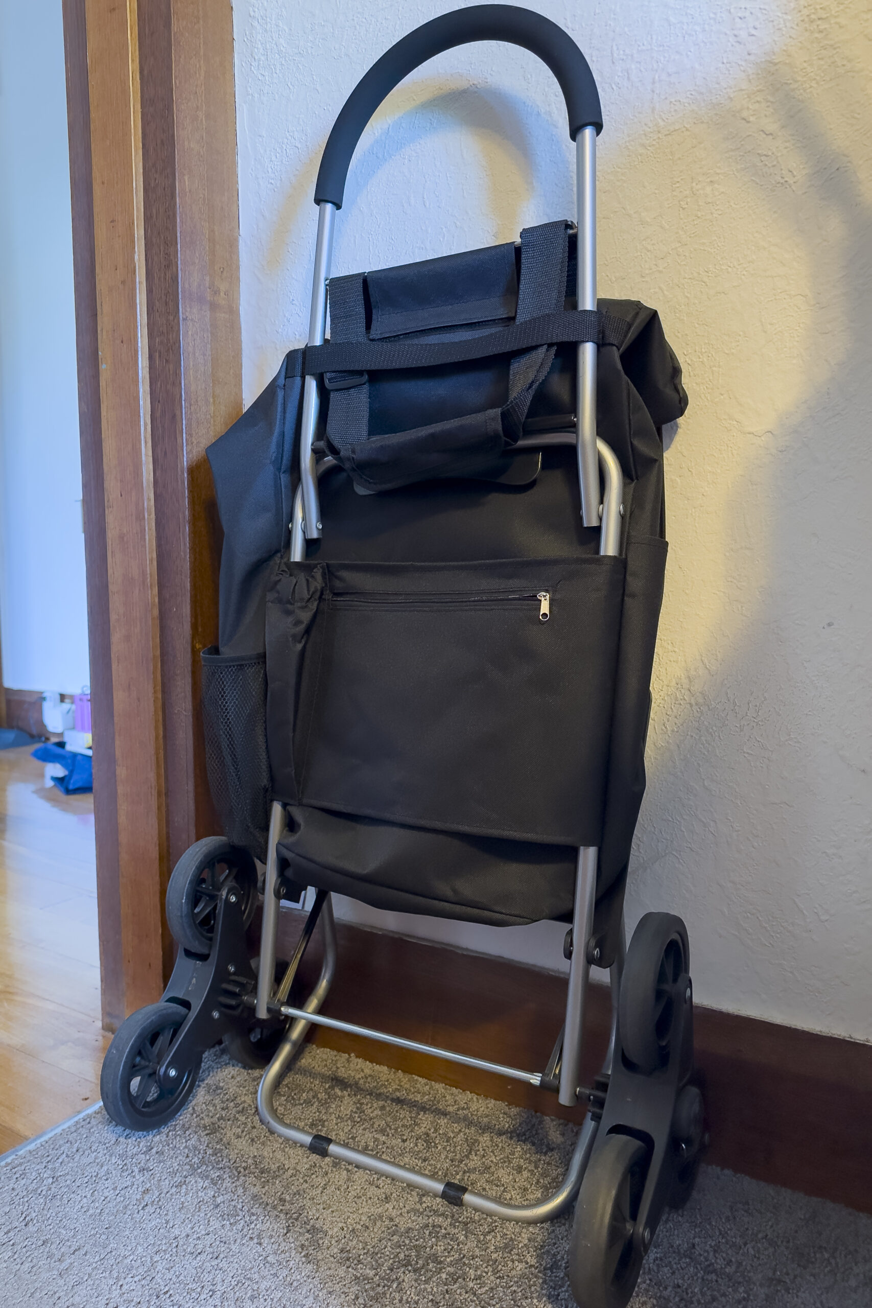 A black shopping trolley folded up and resting against a wall near a doorway