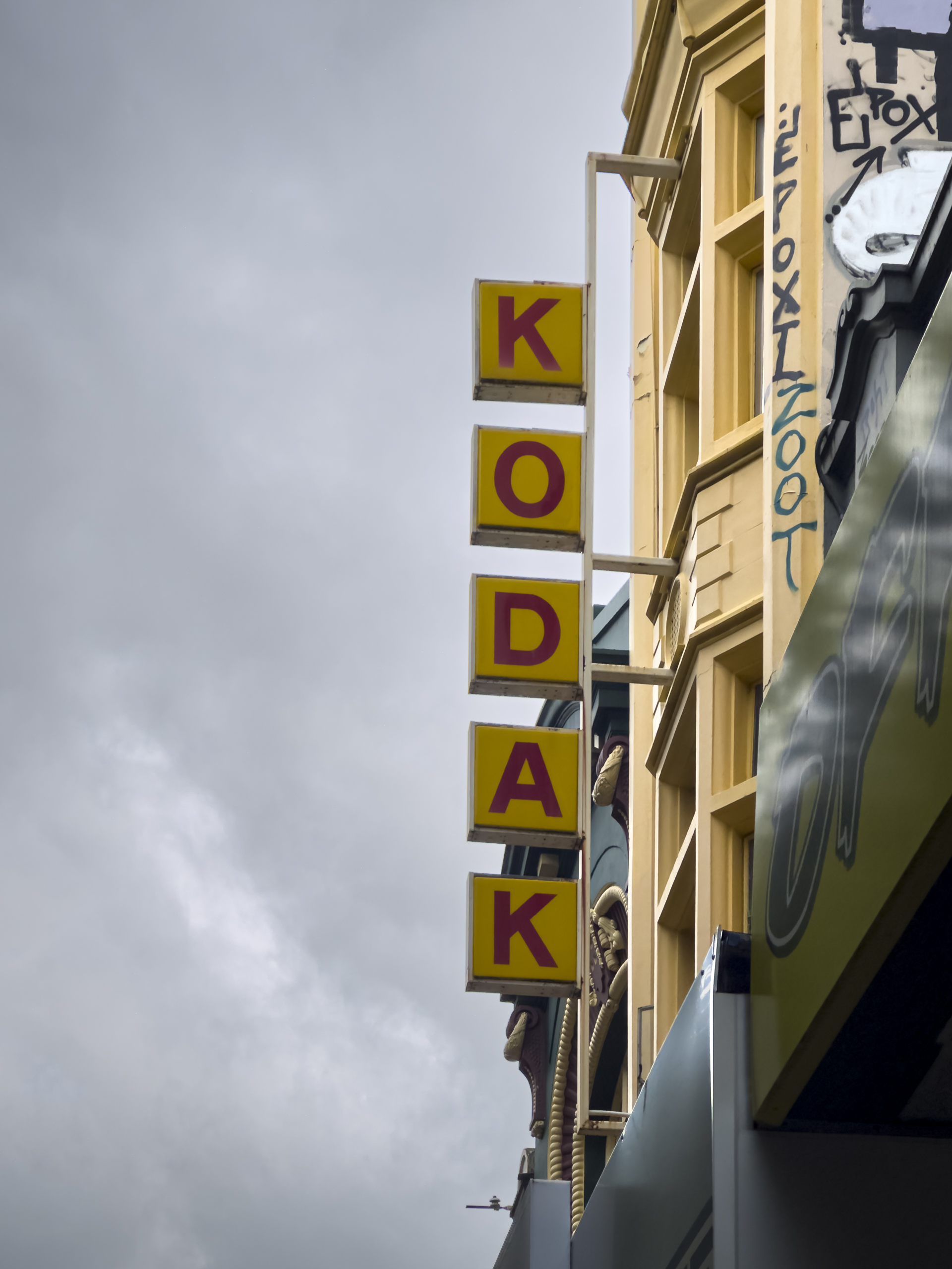 A sign on a building wall comprising red upper case letters within yellow squares spellig out KODAK