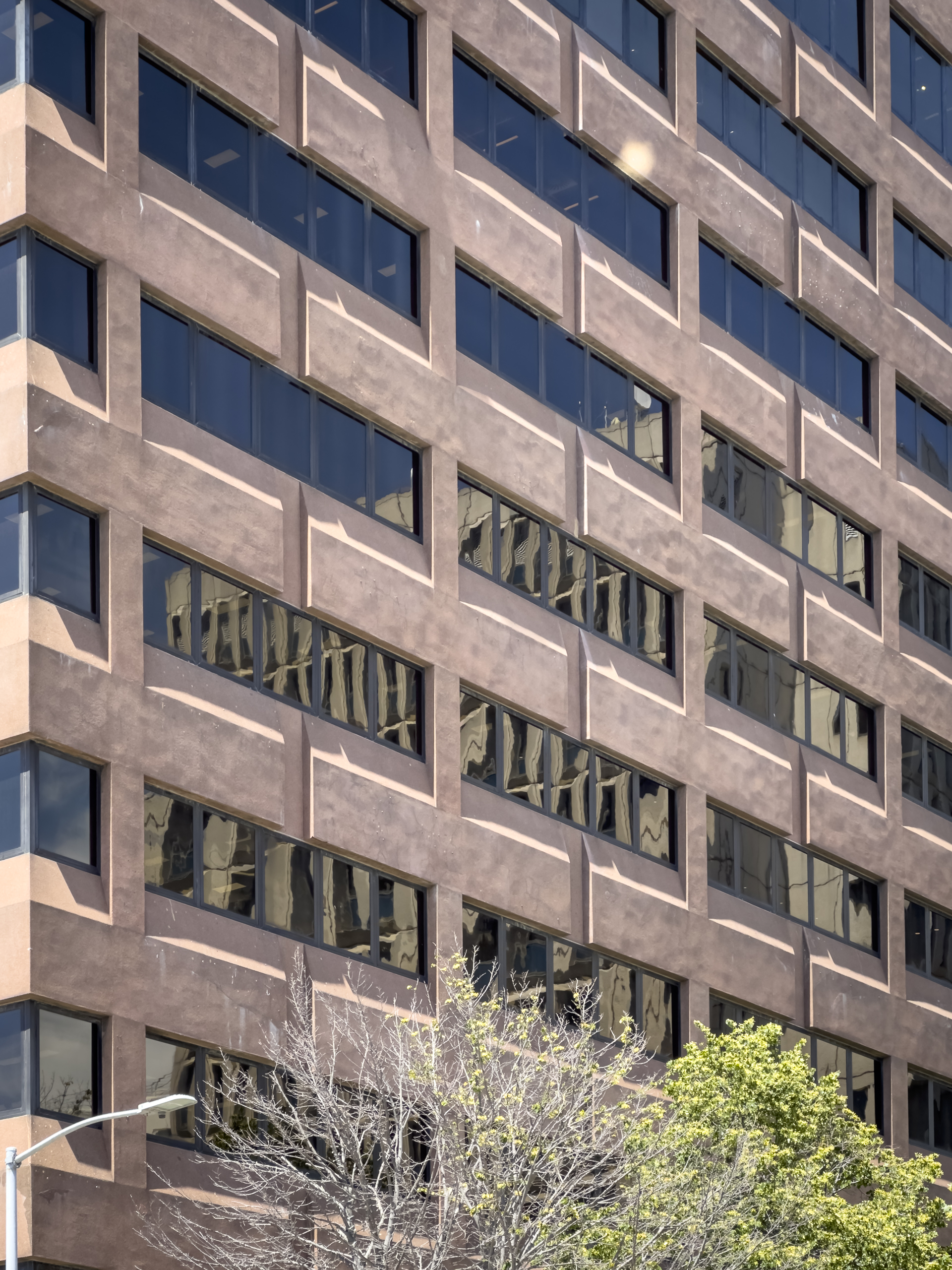 A brown multistorey building with glass windows and the reflection of another multistorey building in the windows