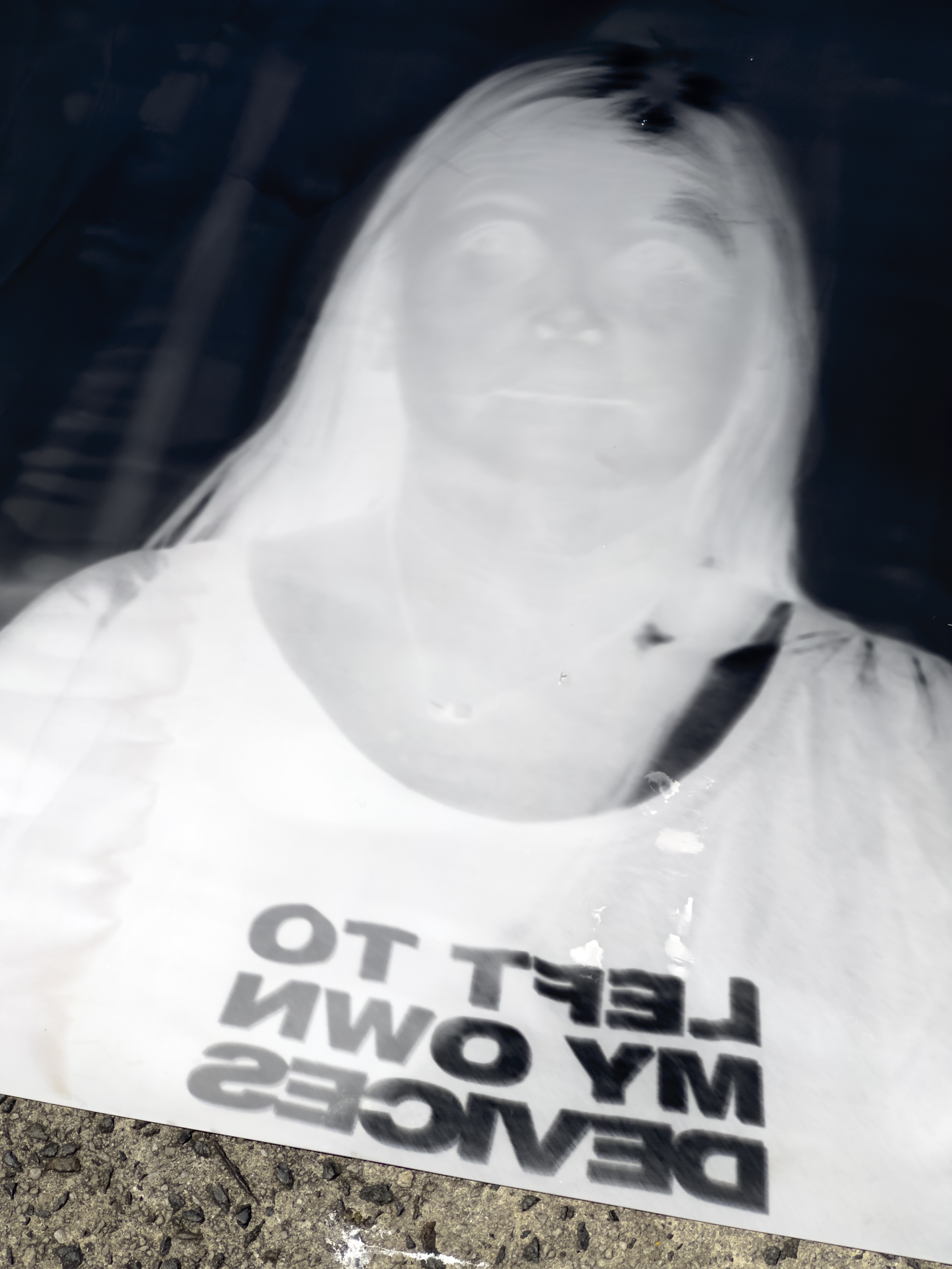 A negative black and white reversed image of a human wearing a shirt that reads LEFT TO MY OWN DEVICES