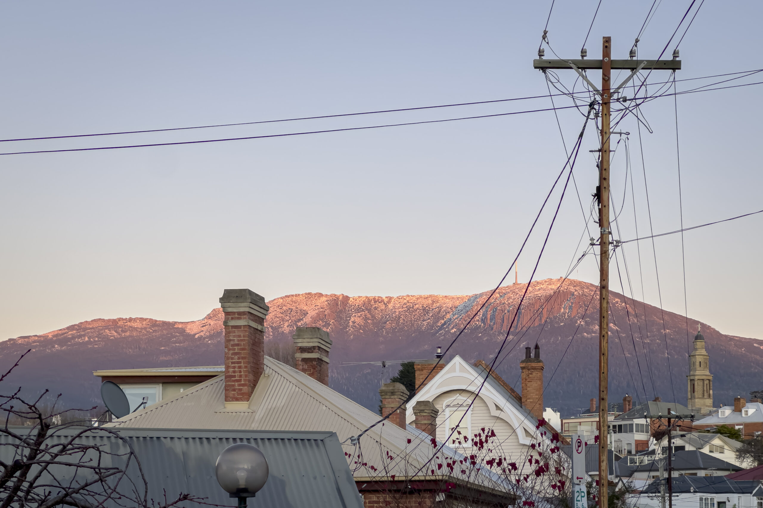 The mountain bathed in pink morning light behind some rooftops and power lines