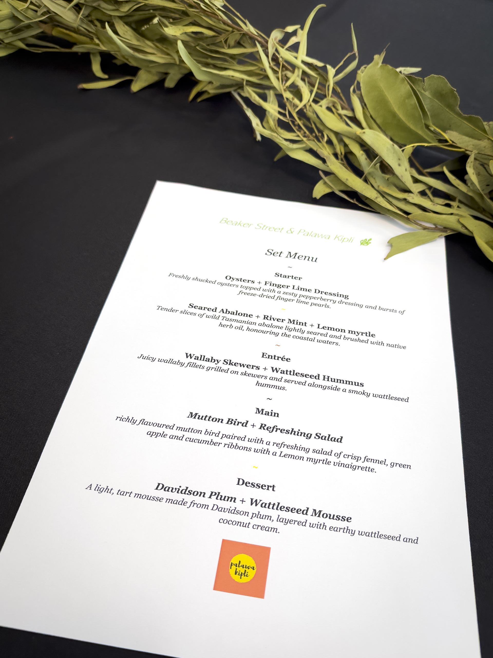 A four-course menu lying on a table with foliage running across the top of the picture