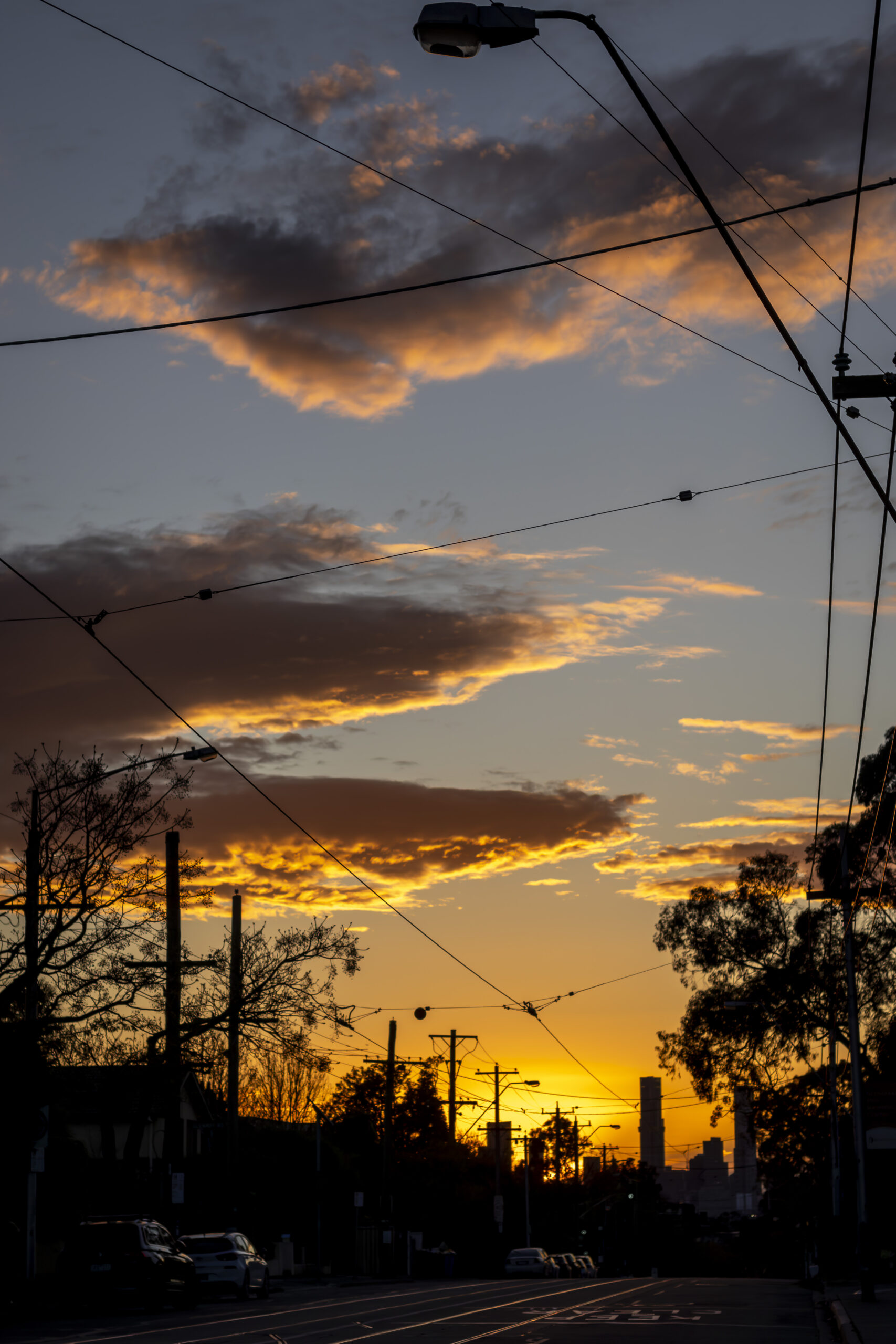 A sunset sky looking back at a city down a darkened road with tram lines
