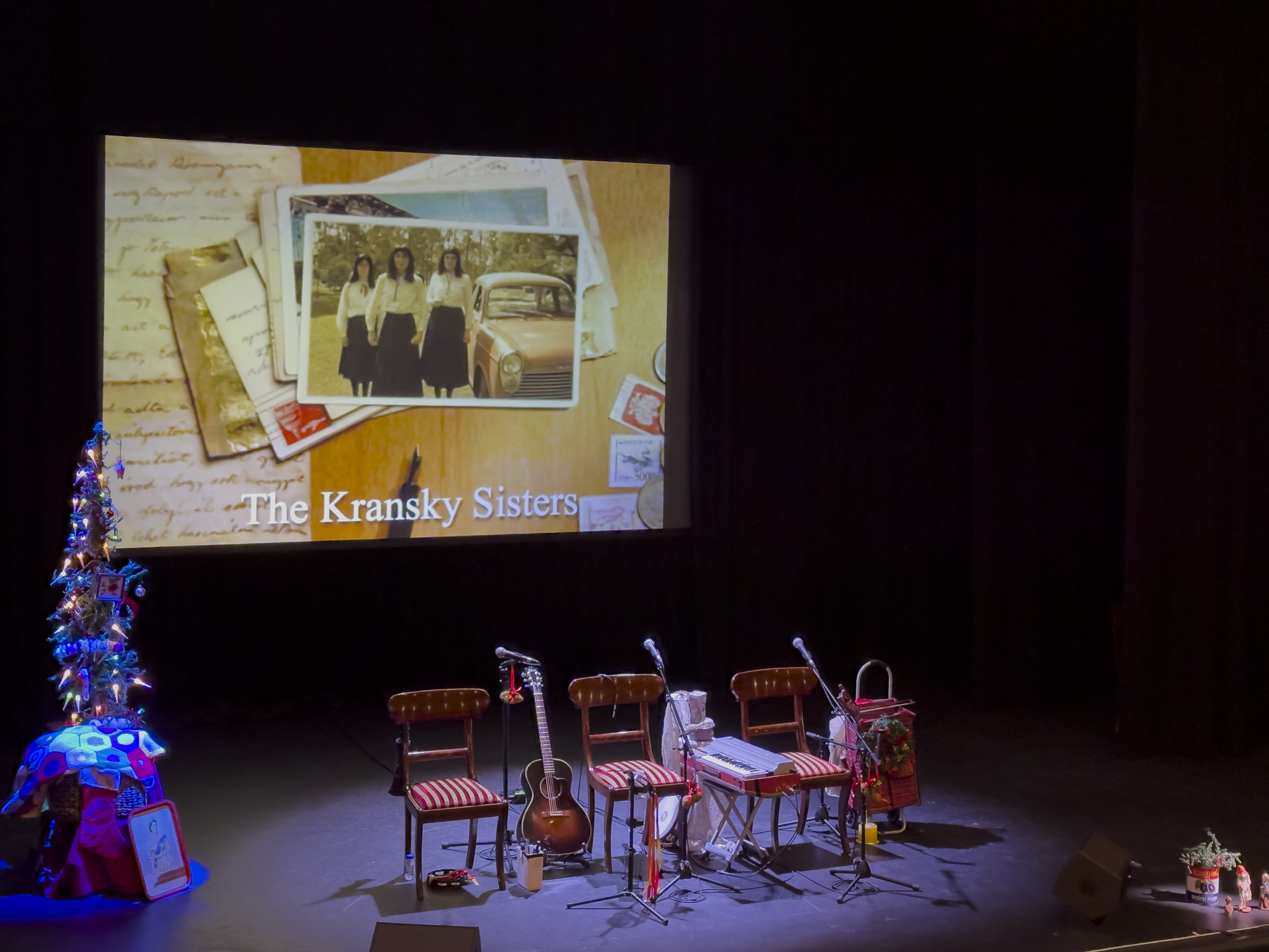 Three chairs set up on a dark stage. There is a slide show playing on the screen behind the chairs