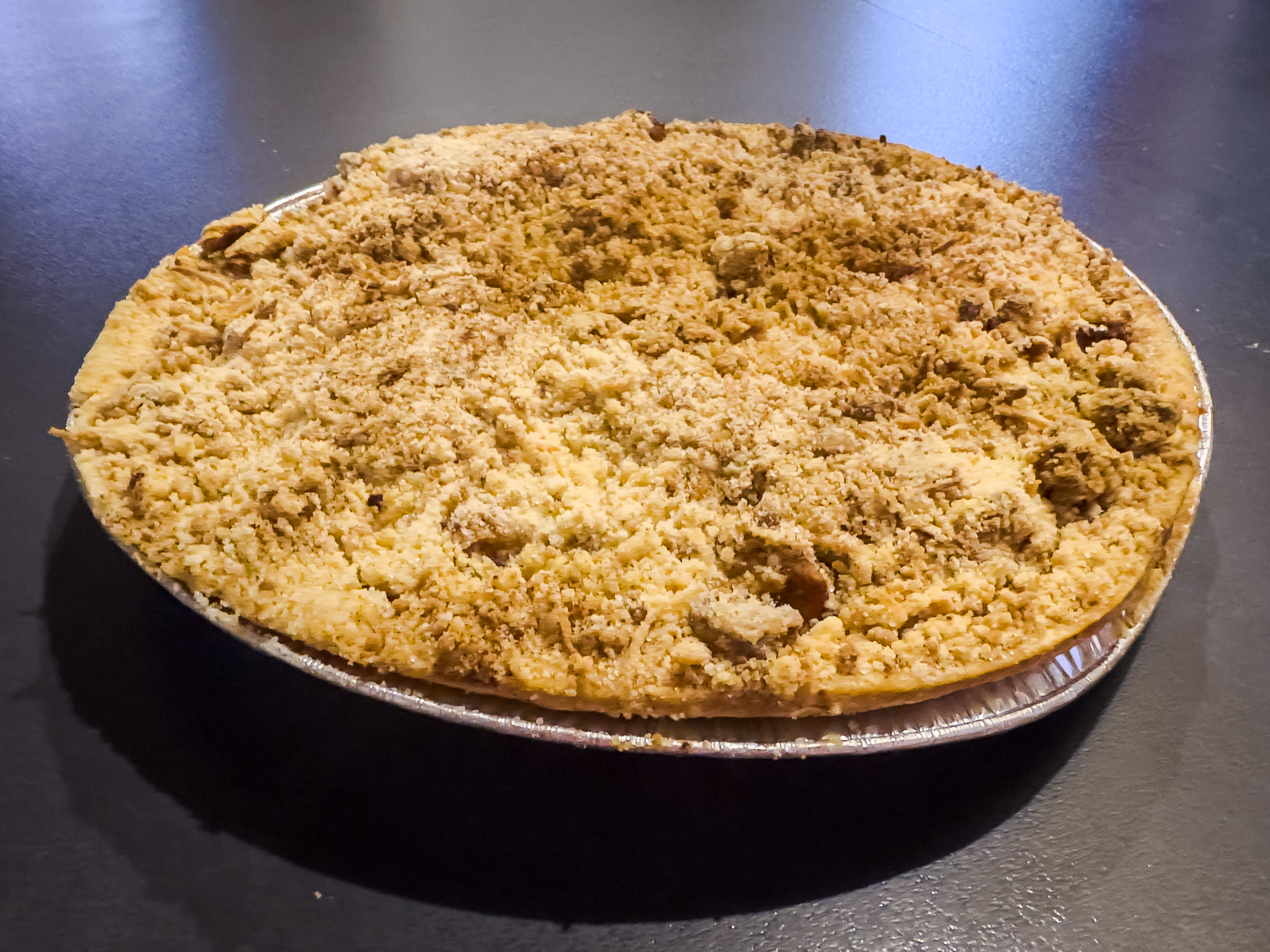 A round crumble-topped pie in a silver foil tray