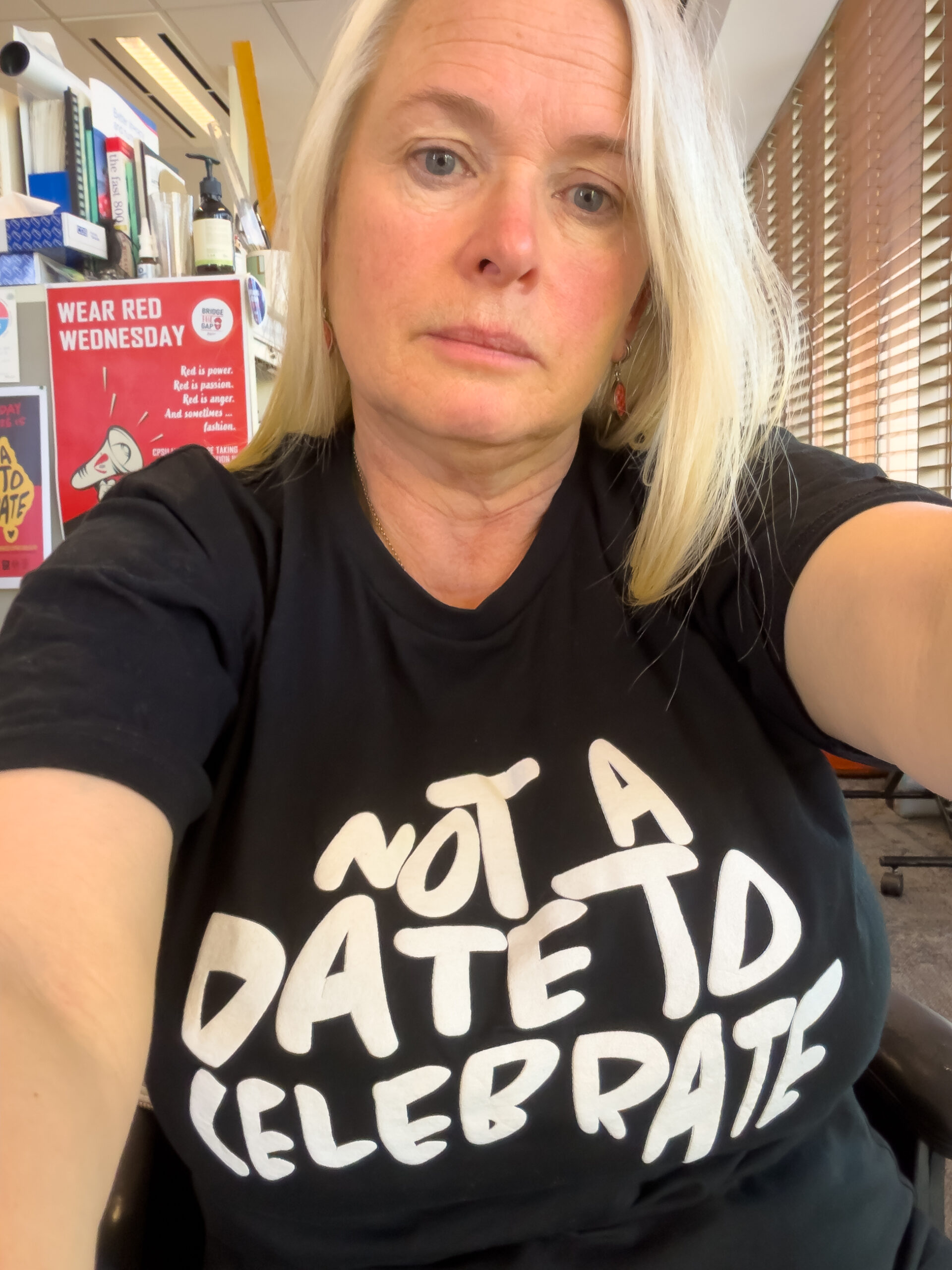 Barb is wearing a black t-sirt that has the text Not a Date to Celebrate in a stylised map of Australia. She is in a workplace
